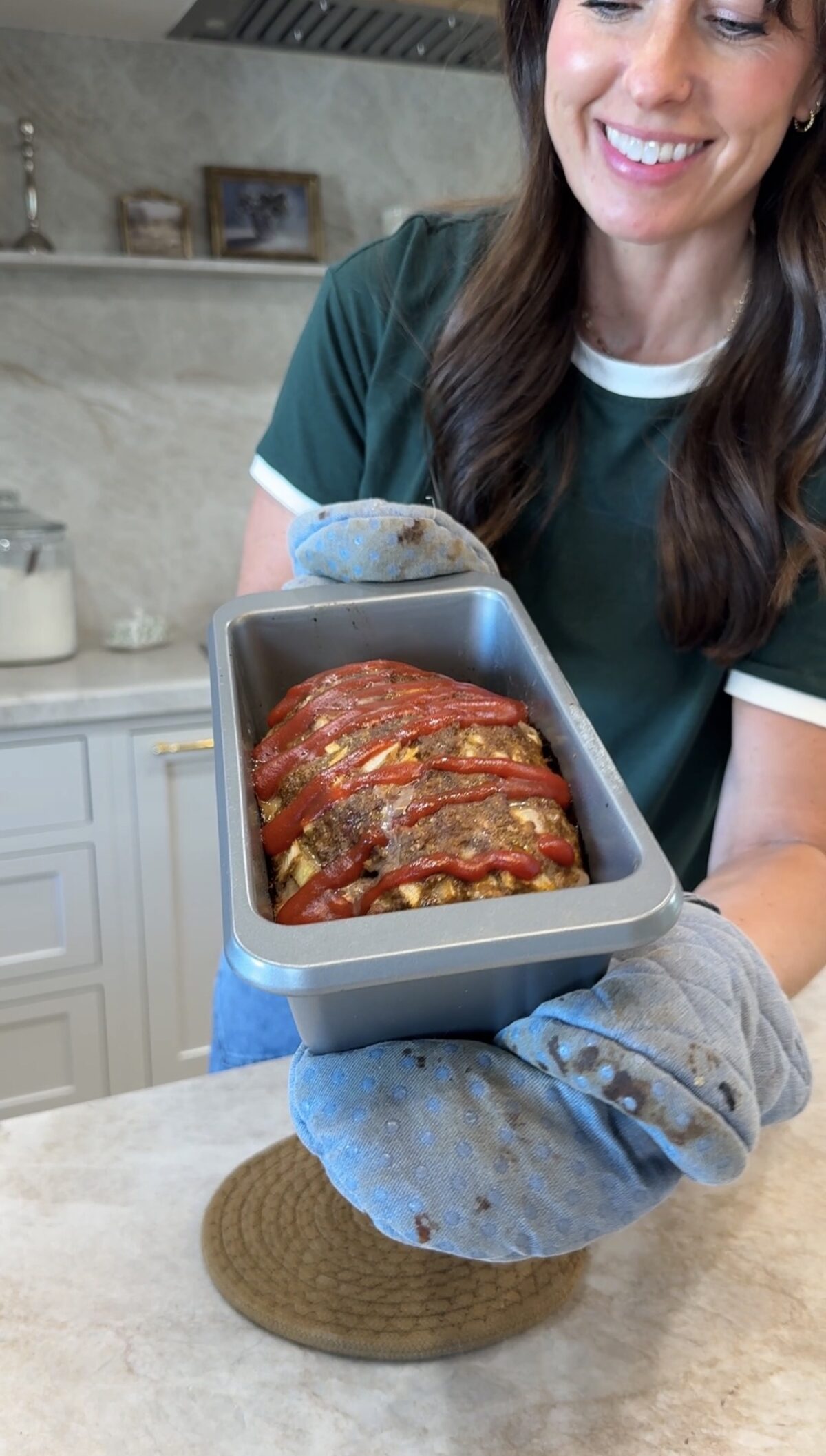 woman showing finished meatloaf with ketchup on top in pan.
