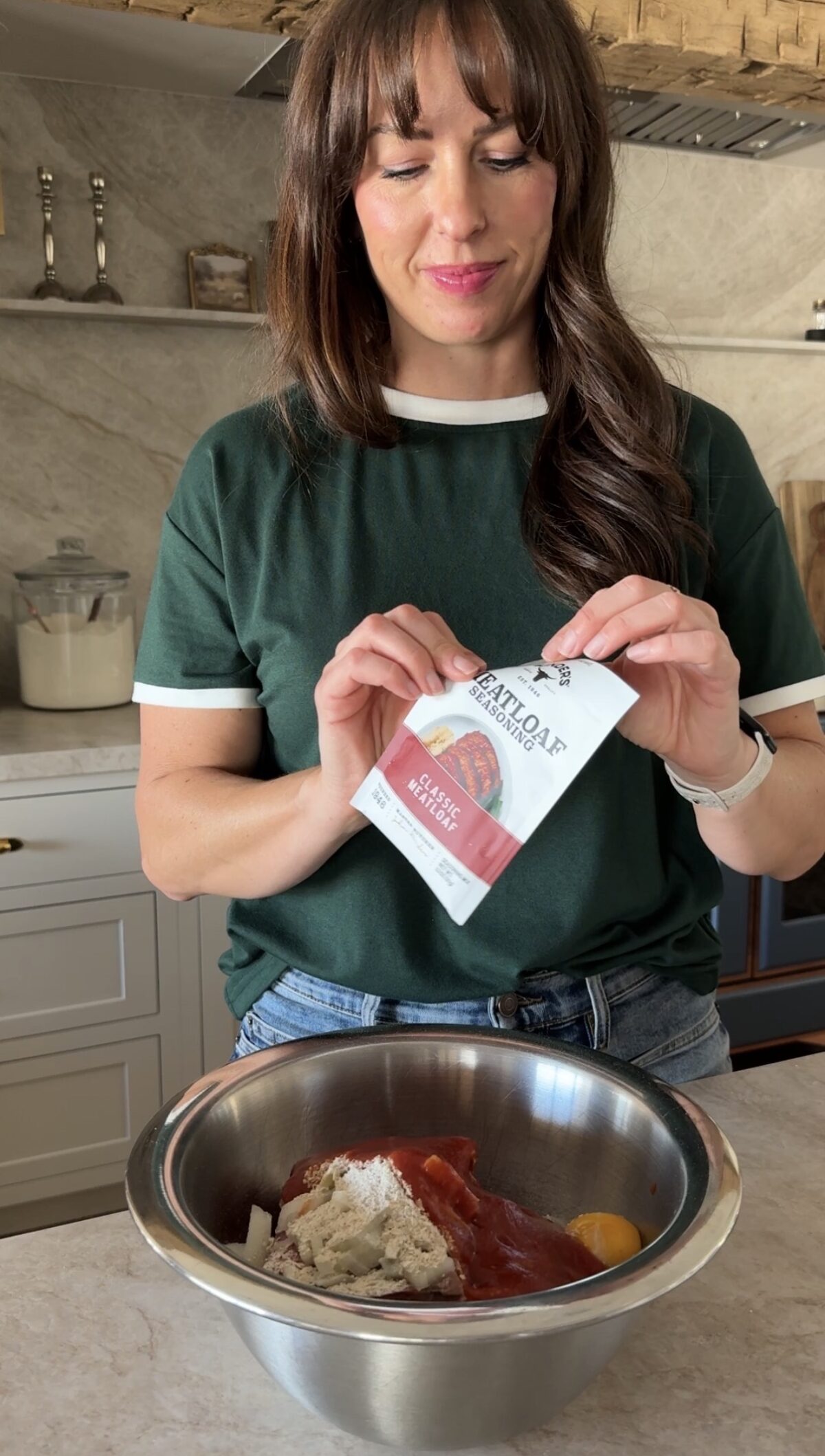 woman making meatloaf with meatloaf seasoning packet. All ingredients are in a mixing bowl.