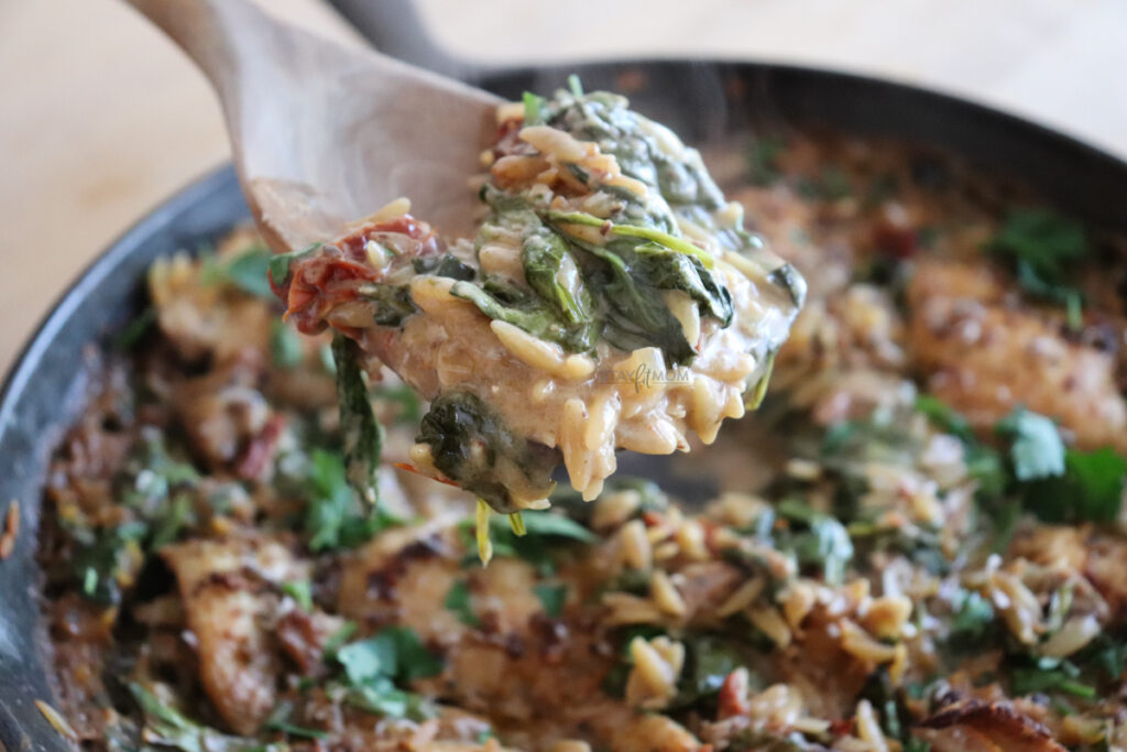 Close up of a scoop of chicken, spinach, sun-dried tomatoes and orzo in one dish.