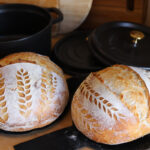 Beautiful sourdough bread with leaf designs in front of dutch oven pans.