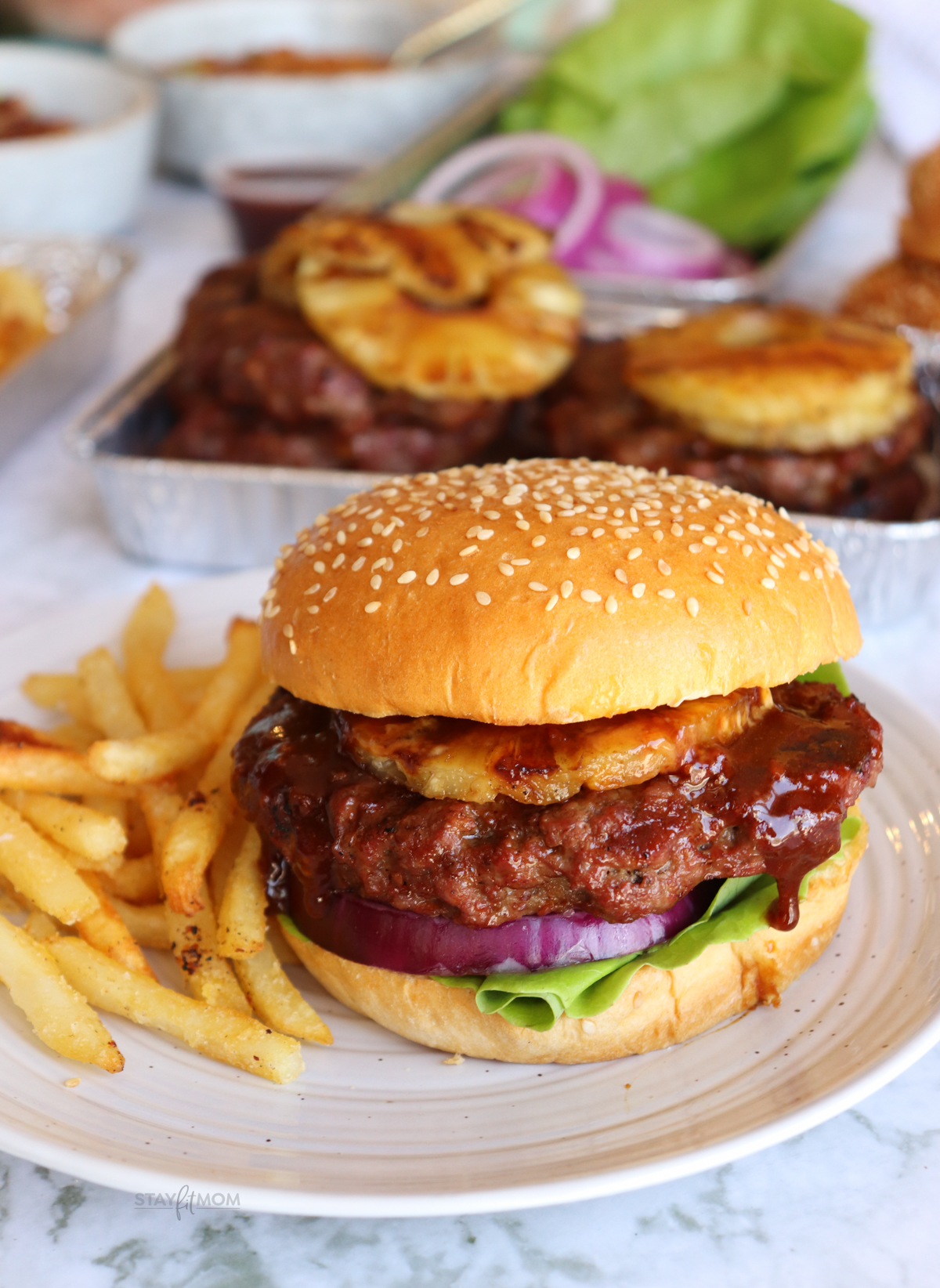 Teriyaki Burger on a bun with visible grilled burger topped with pineapple, lettuce, onions, and a side of fries.