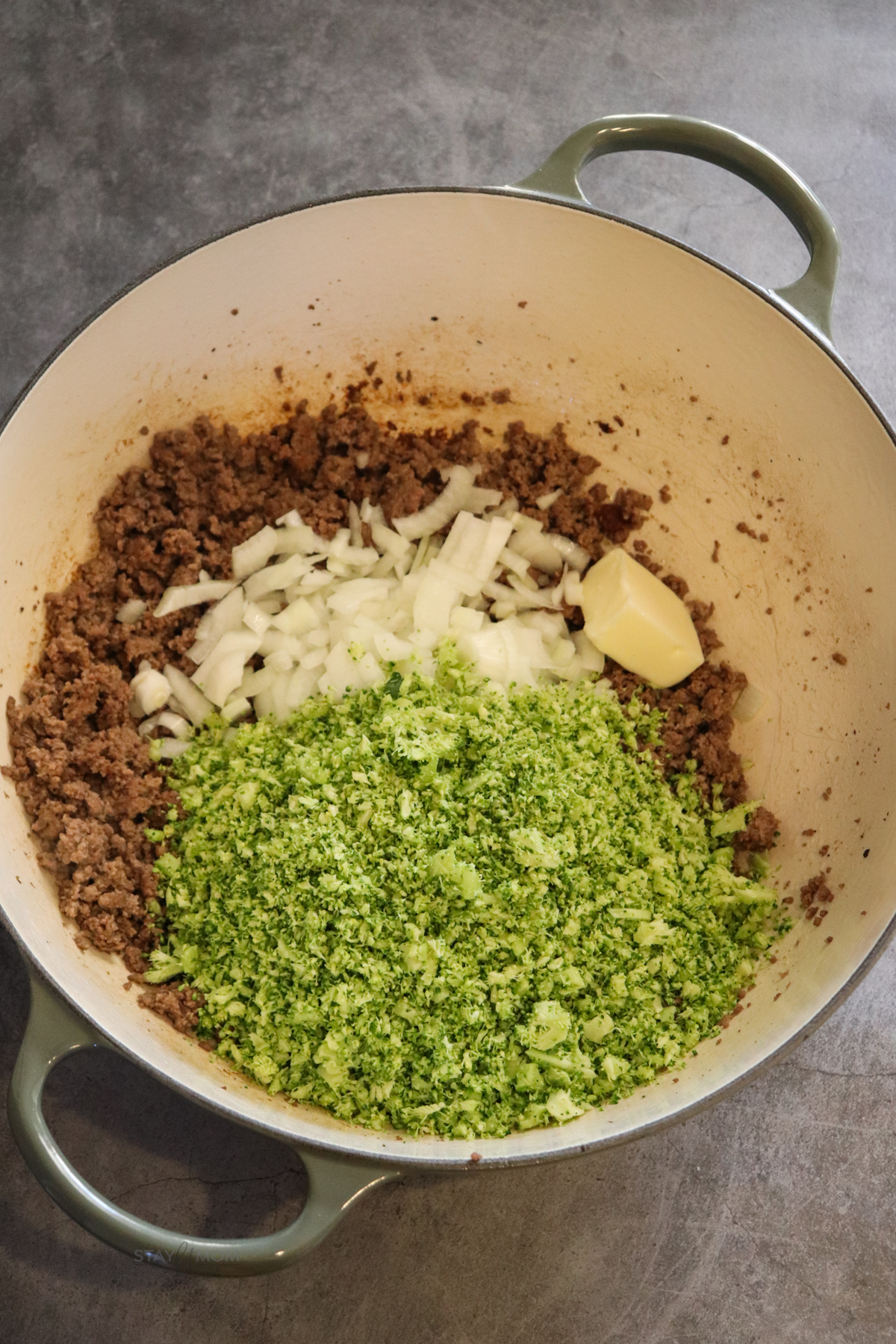 Beefy Alfredo Mac Image of large pot containing cooked ground beef topped with onions, broccoli, and butter.