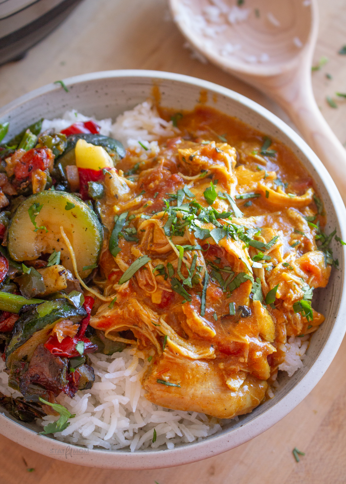 Butter chicken showing sauce with chicken and veggies over rice.