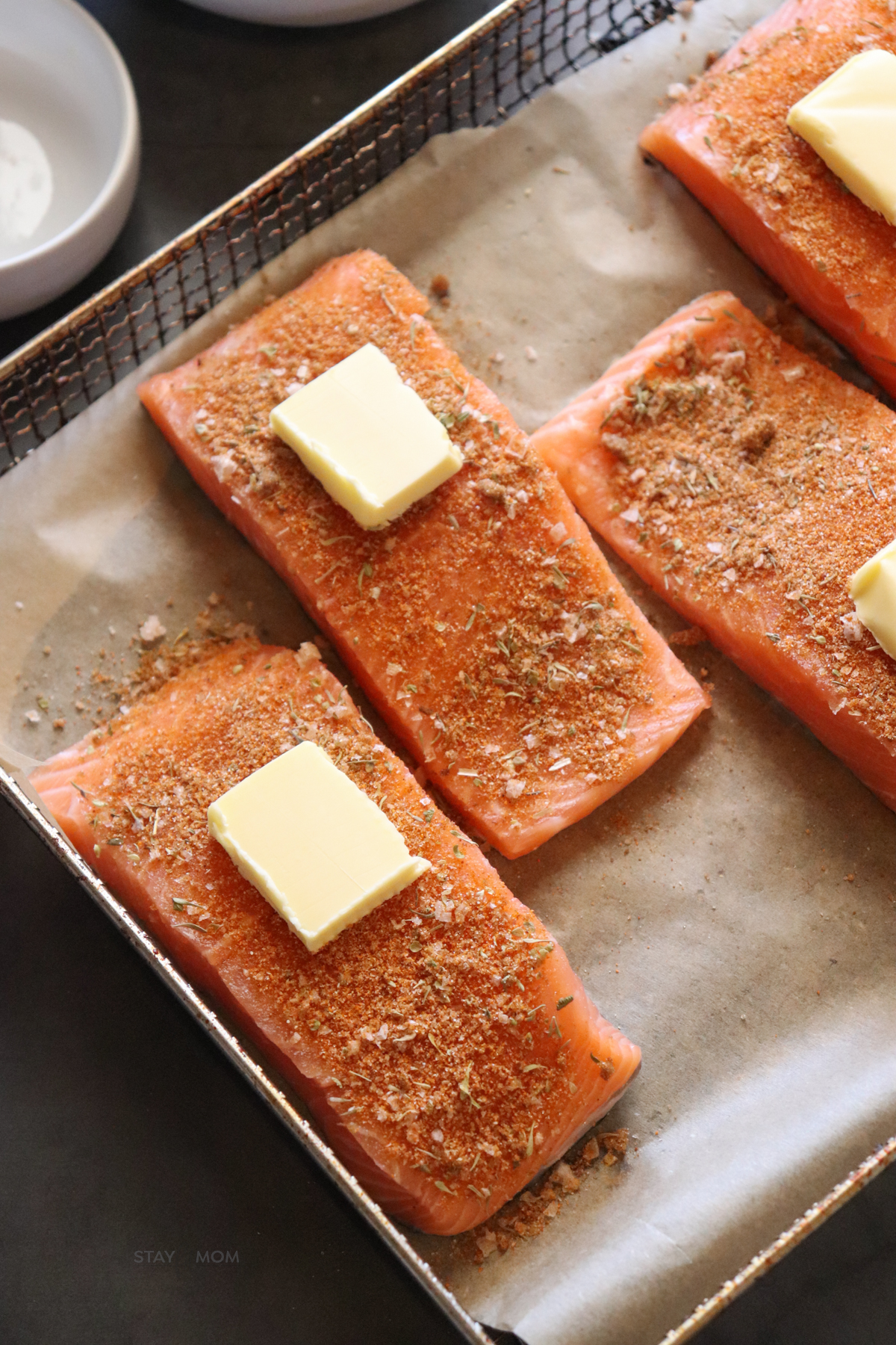 Salmon coated in spices with a pat of butter on top ready to be air fryed.