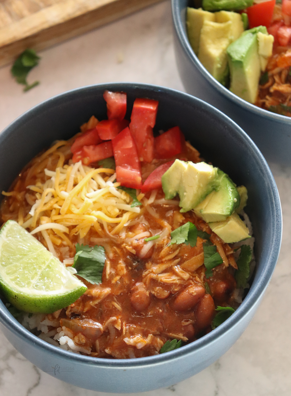 Enchilada Stew showing completed meal topped with cheese, tomatoes, avocados, lime, and cilantro.