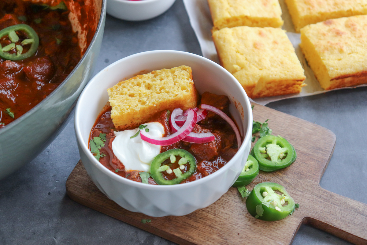 Texas chili showing a serving of coup topped with onions, sour cream, cilantro, jalapenos, and cornbread.
