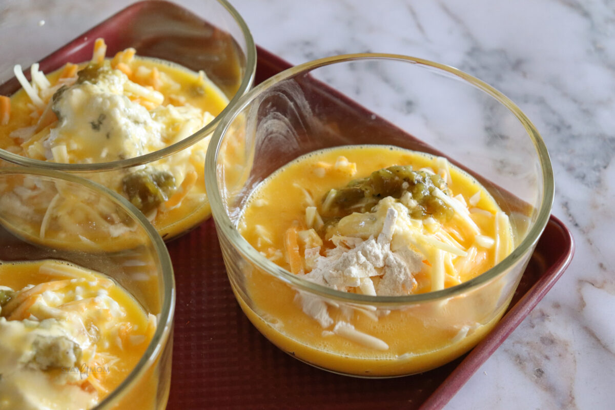 Green Chile Egg Casseroles showing baking sheet with 5 meal prep bowls ready to be stirred and baked.