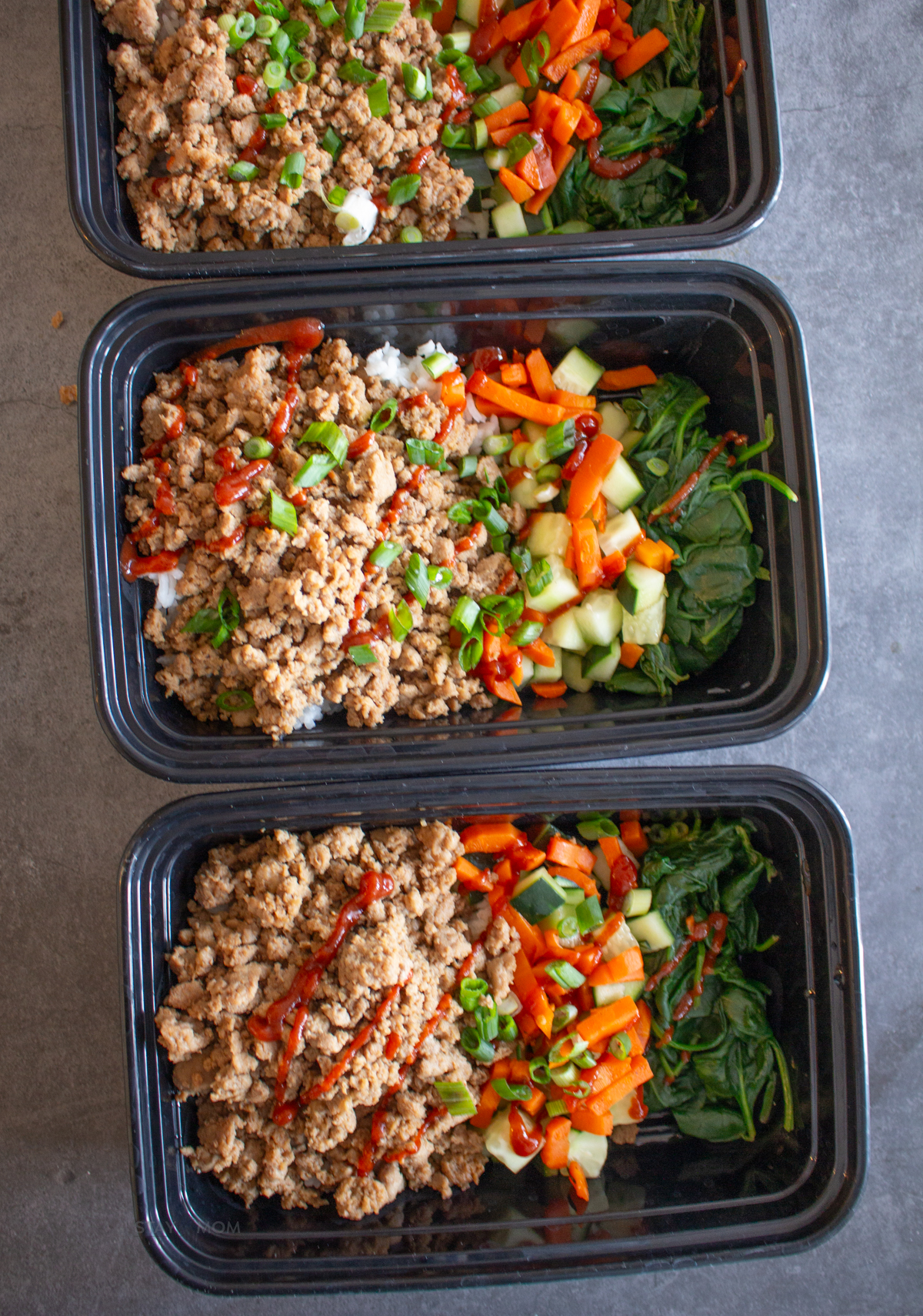 Korean Ground Turkey bowls showing finished meal with ground turkey, rice, veggies, and topped with green onions and extra Sriracha.