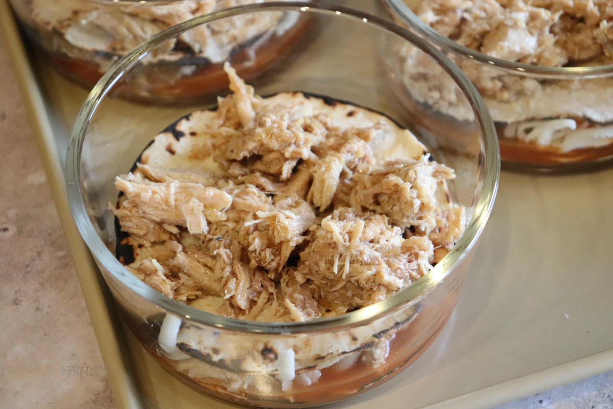 Pork Enchilada Bowls showing meal prep bowl with a layer of enchilada sauce, tortilla, and shredded pork.