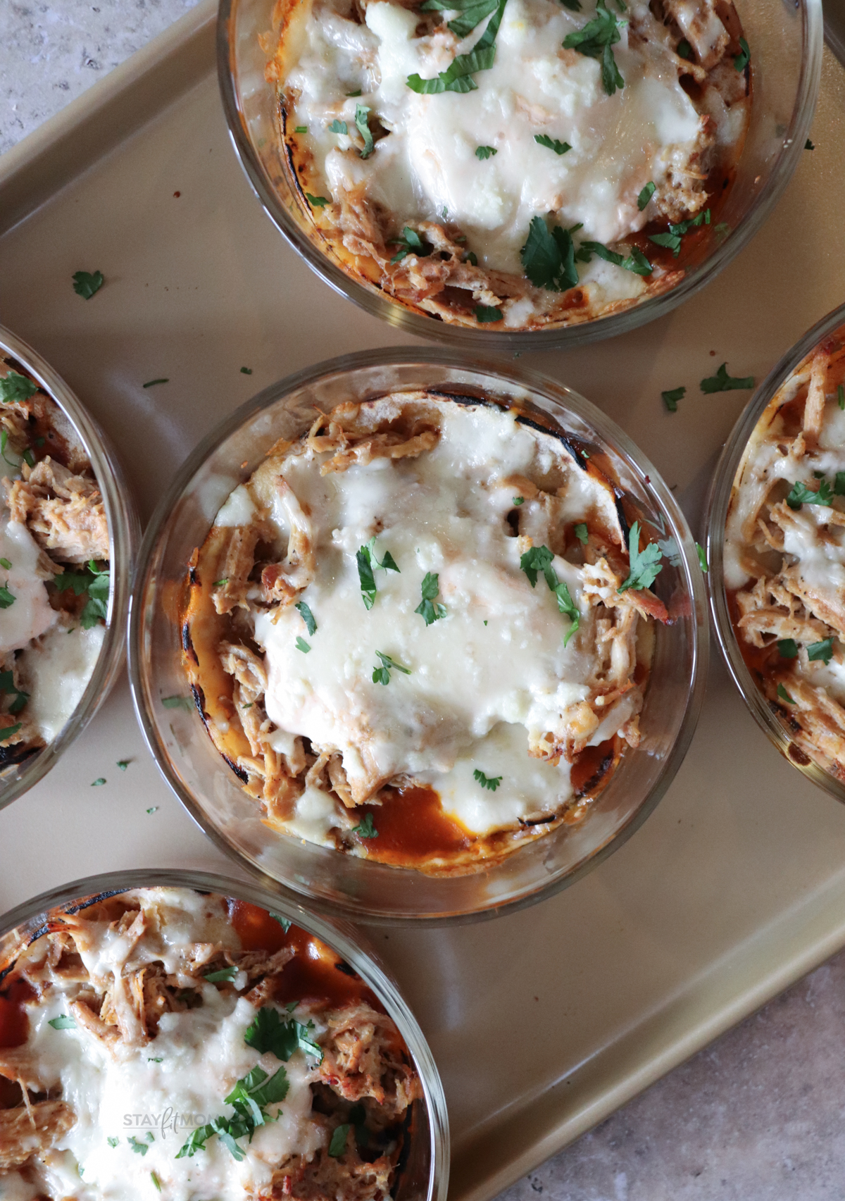 Pork Enchilada bowls showing finished meal prep recipe with visible melted cheese, shredded pork, red enchilada sauce, and corn tortillas.