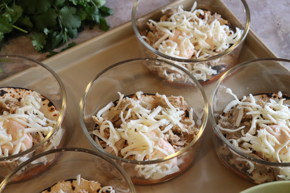 Pork Enchilada Bowls showing meal prep bowl with a layer of enchilada sauce, tortilla, shredded pork, and topped with cheese ready to bake.