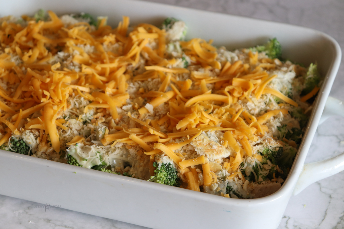 Chicken divan prepared and ready to bake with visible chicken, broccoli, sauce, crushed crackers, and shredded cheese.