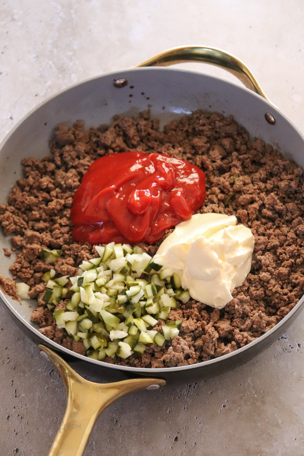 Cheeseburger Sloppy Joes showing skillet with cooked ground beef topped with ketchup low fat mayo, and pickles ready to be stirred in.