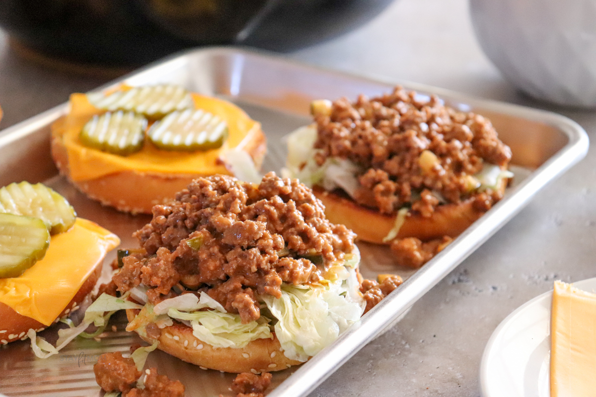 Open faced Cheeseburger Sloppy Joes showing buns piled with lettuce and sloppy joe meat an top buns toasted with American cheese and picklles.