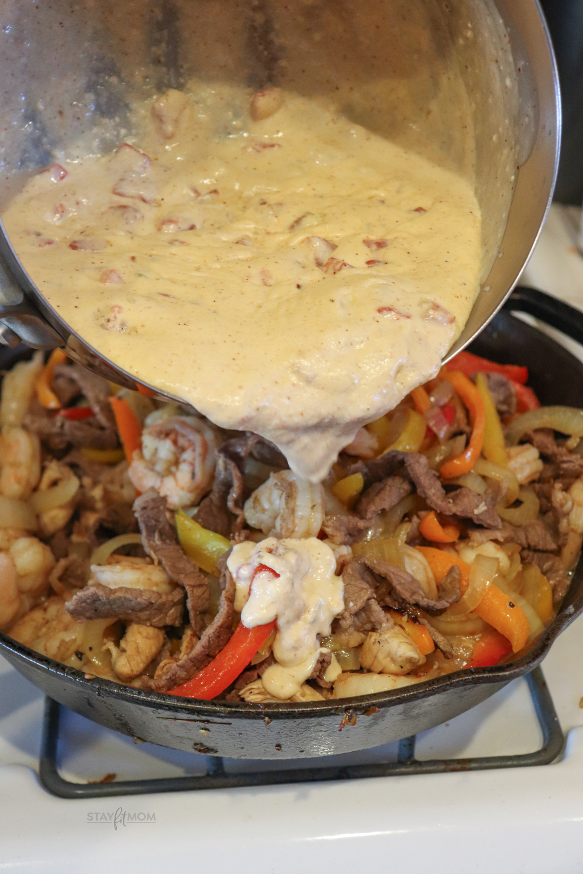 3 Meat Queso Skillet showing queso being poured onto meat and veggie mixture.