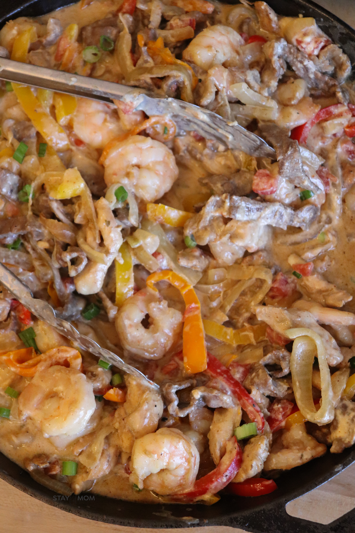 3 Meat Queso Skillet showing completed meal on a plate with visible shrimp, chicken, steak, peppers, onions all coated in a creamy queso.