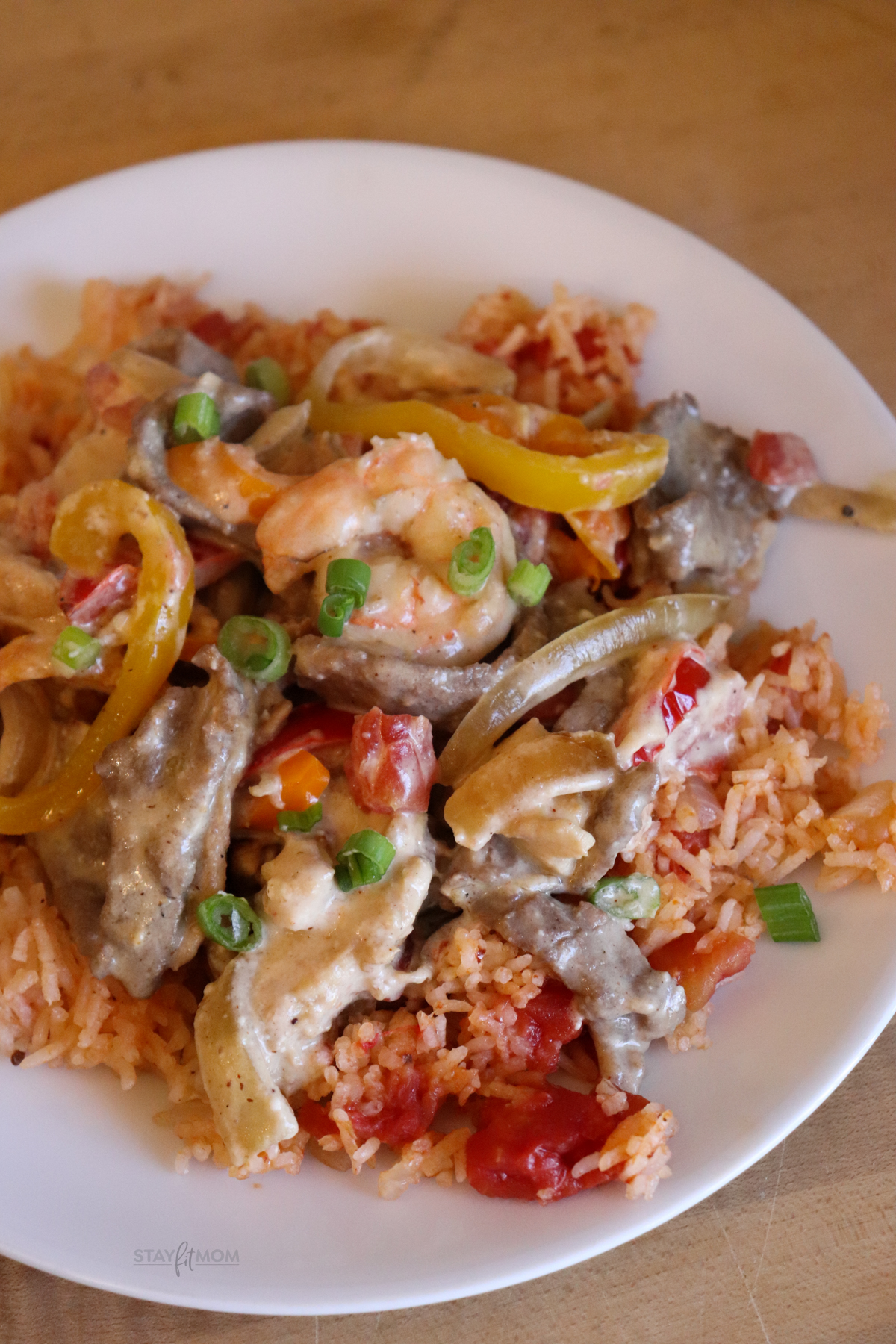 3 Meat Queso Skillet showing completed meal on a plate with visible rice, shrimp, chicken, steak, peppers, onions all coated in a creamy queso.