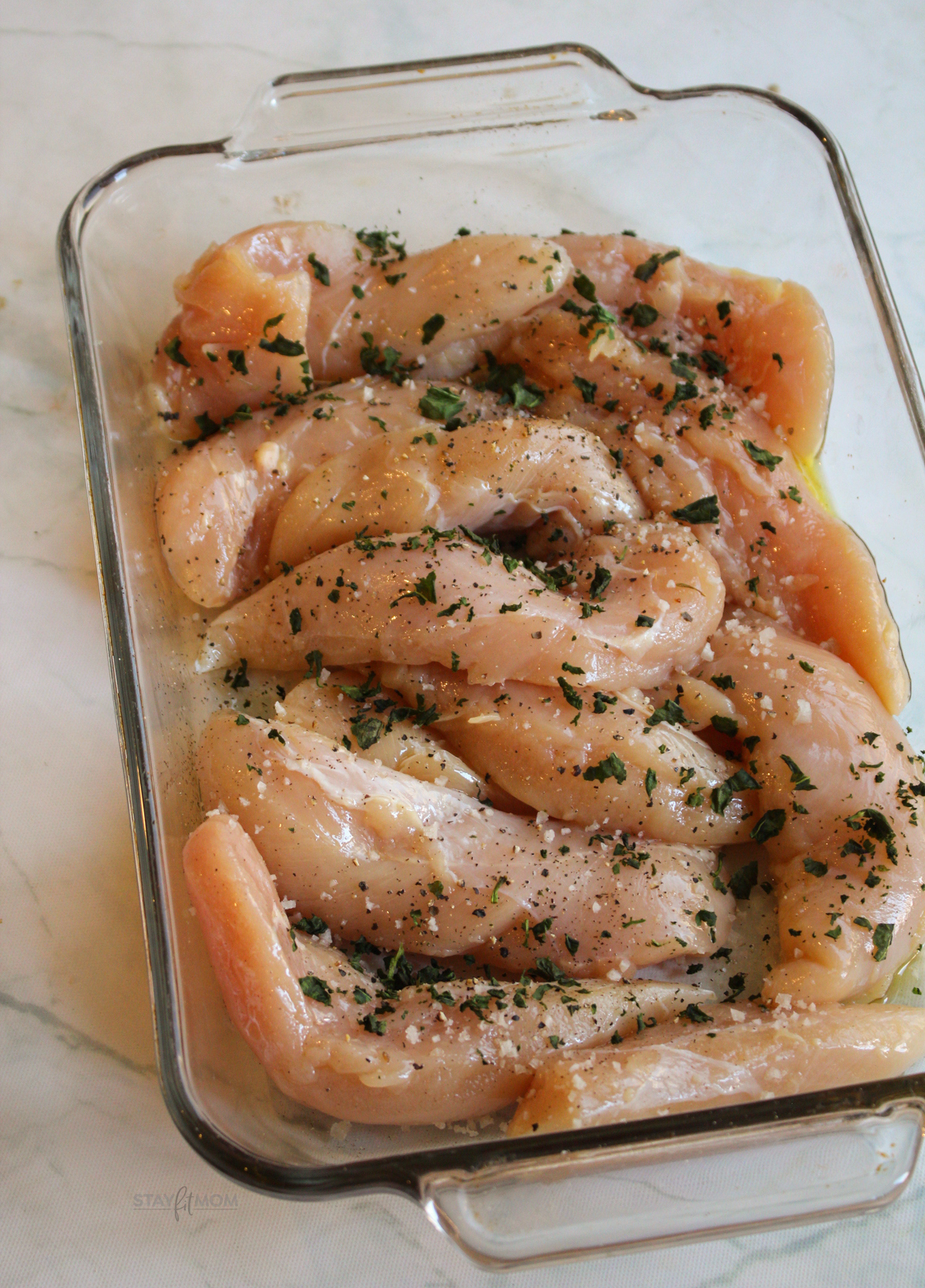 Creamy Garlic Basil Chicken showing baking dish with seasoned chicken tenders ready to be cooked.