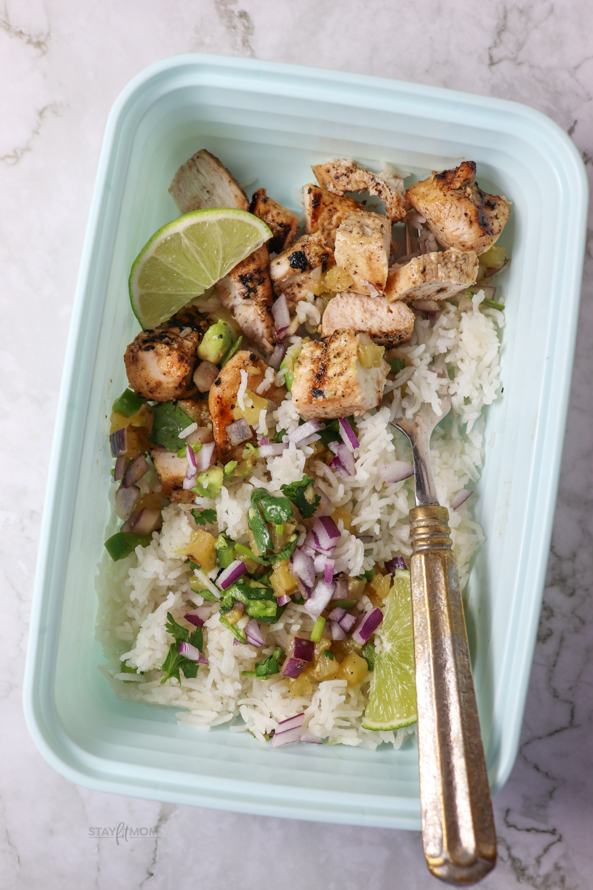 Close up view of Hawaiian Chicken Bowls showing rice and chicken topped with pineapple salsa and a lime wedge.