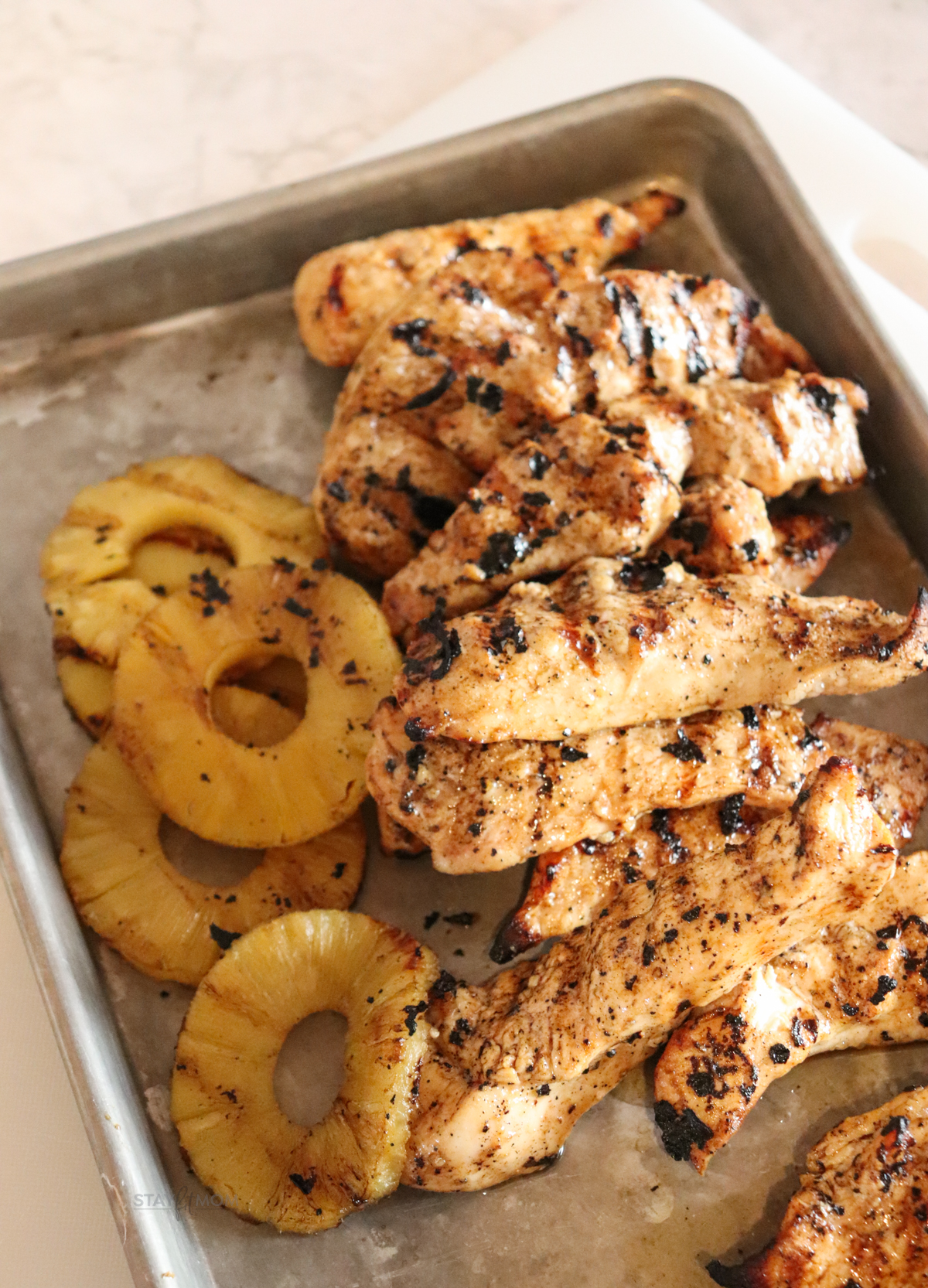 Hawaiian Chicken Bowls showing pan loaded with marinated grilled chicken pieces and grilled pineapple rings.