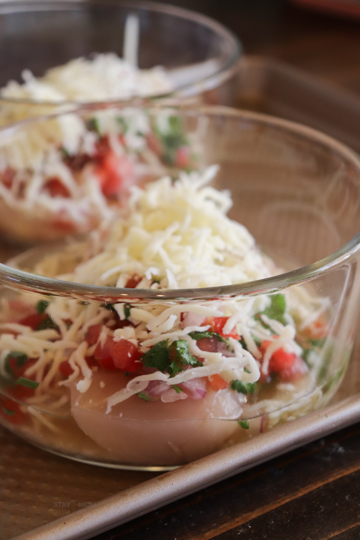 Salsa Fresca Chicken Bakes showing glass bowl with visible broth, chicken breast, fresh salsa, rice, and mozzarella ready to be baked.