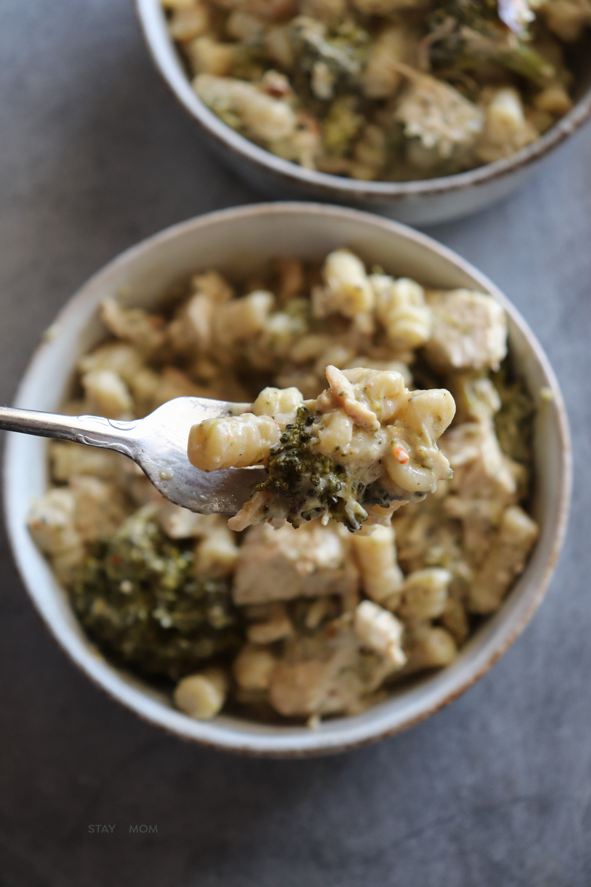 Chicken Parmesan pasta showing a perfect bite over a serving with visible pasta, broccoli, chicken, and creamy sauce.