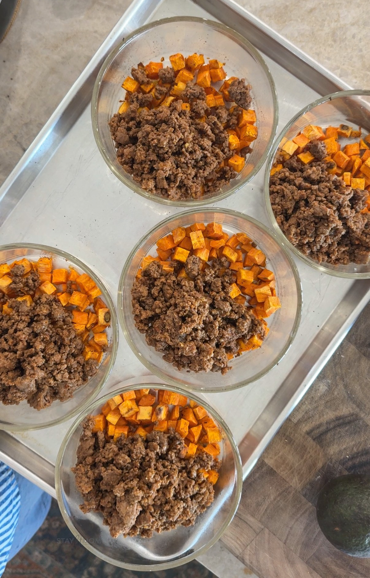 Hot honey sweet potato bowls with 5 Meal prep bowls on a cookie sheet filled with diced sweet potatoes and ground beef seasoned with spices.
