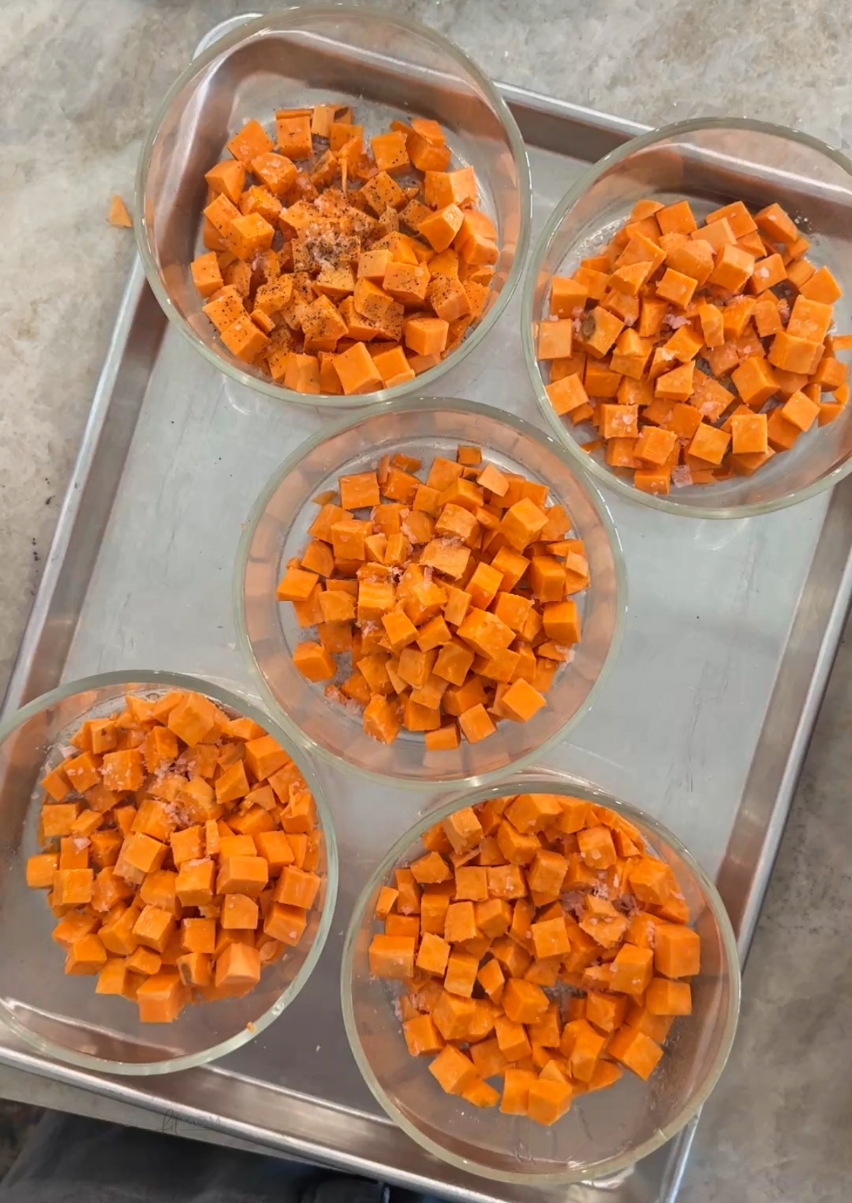 Hot Honey Sweet Potato Bowls Meal prep bowls with diced sweet potatoes sprinkled with salt on a baking sheet.