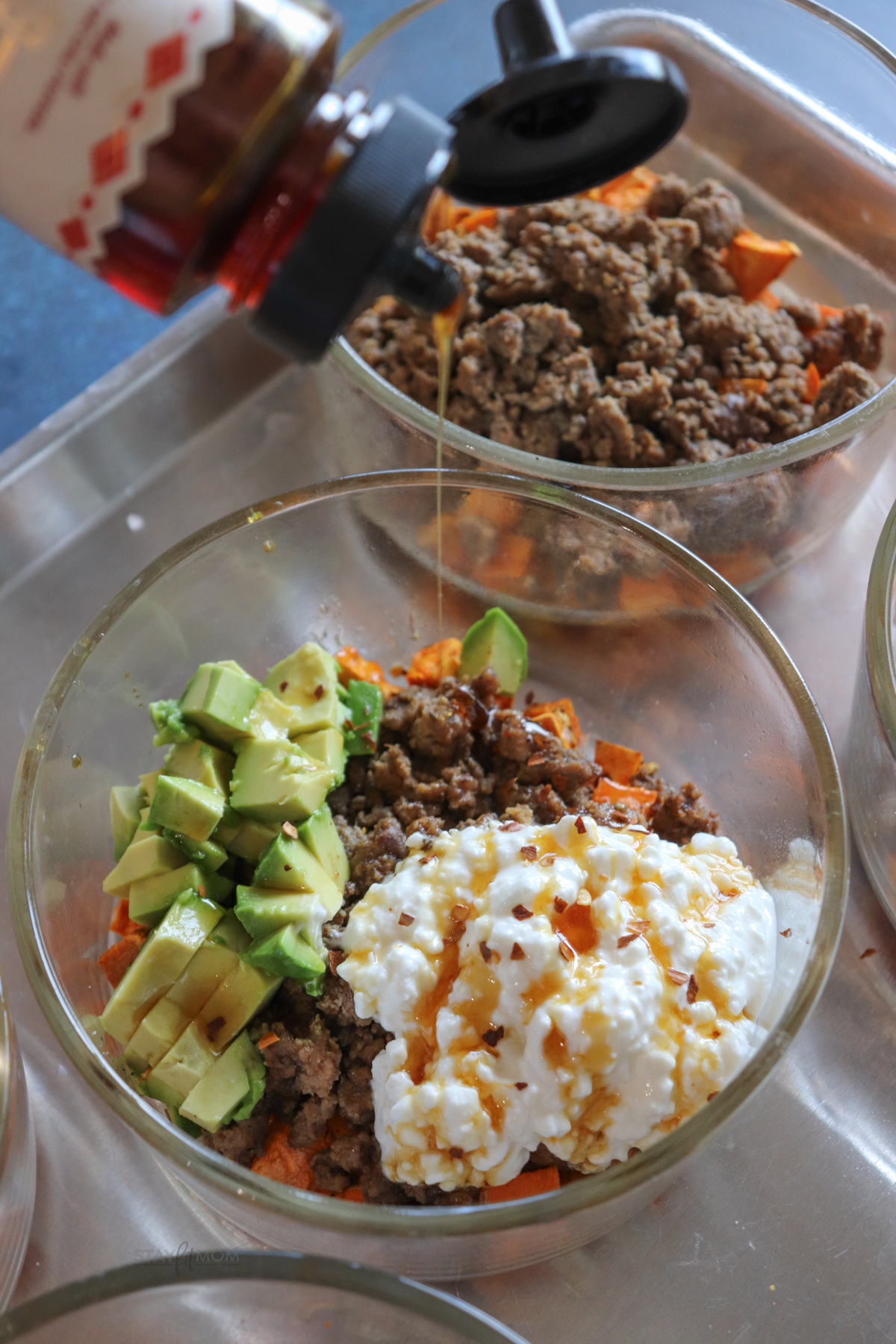 Hot honey sweet potato bowls showing a competed meal with visible sweet potatoes, ground beef, cottage cheese, avocado, and a drizzle of hot hoey.