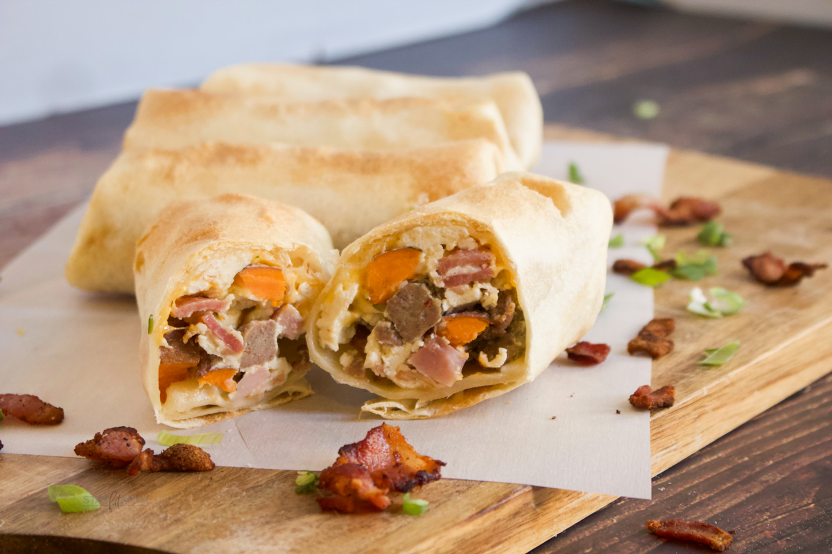Meat Lovers Breakfast Burritos showing completed Burritos and one cut in half to show inside with visible turkey sausage, bacon, ham, and eggs.