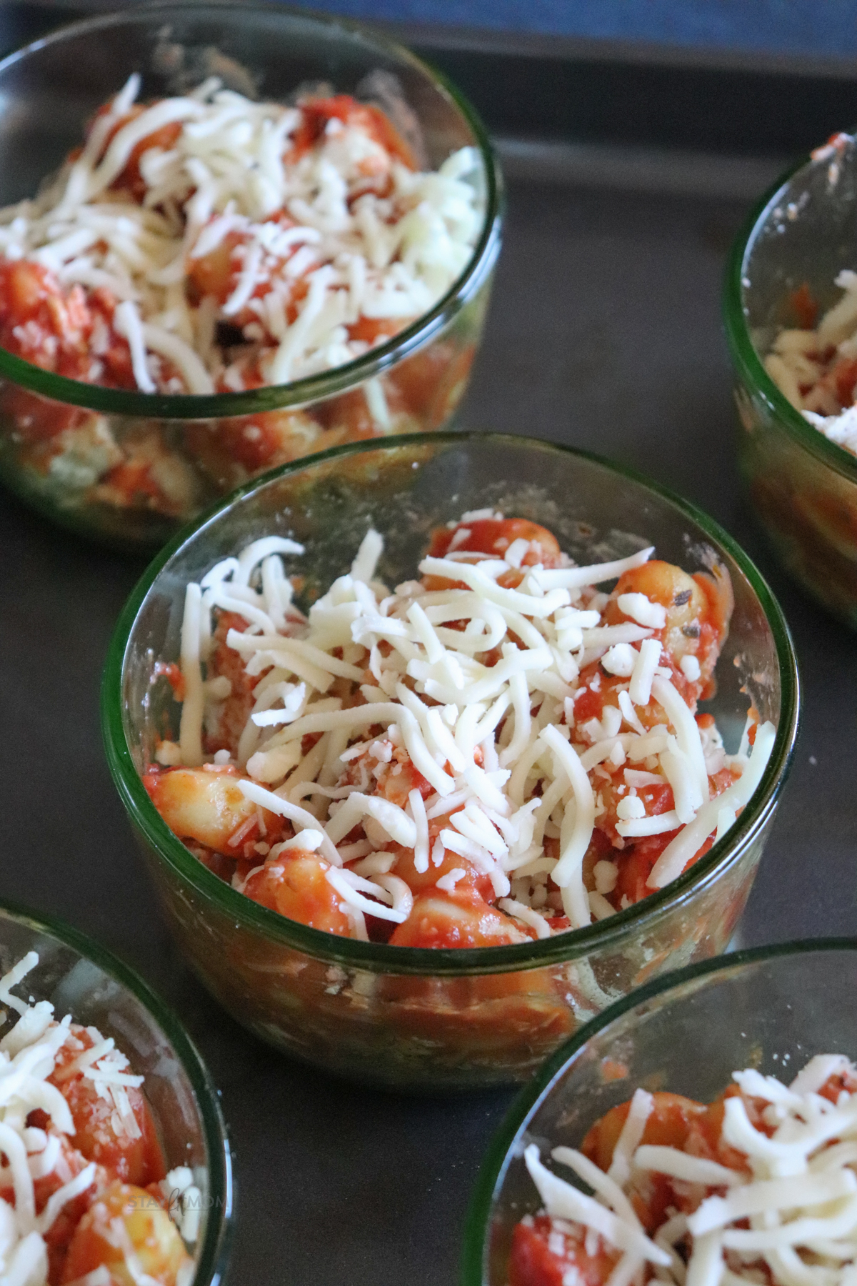 Five oven-safe glass containers filled with gnocchi, chicken, sauce, and topped with shredded mozzarella and parmesan.