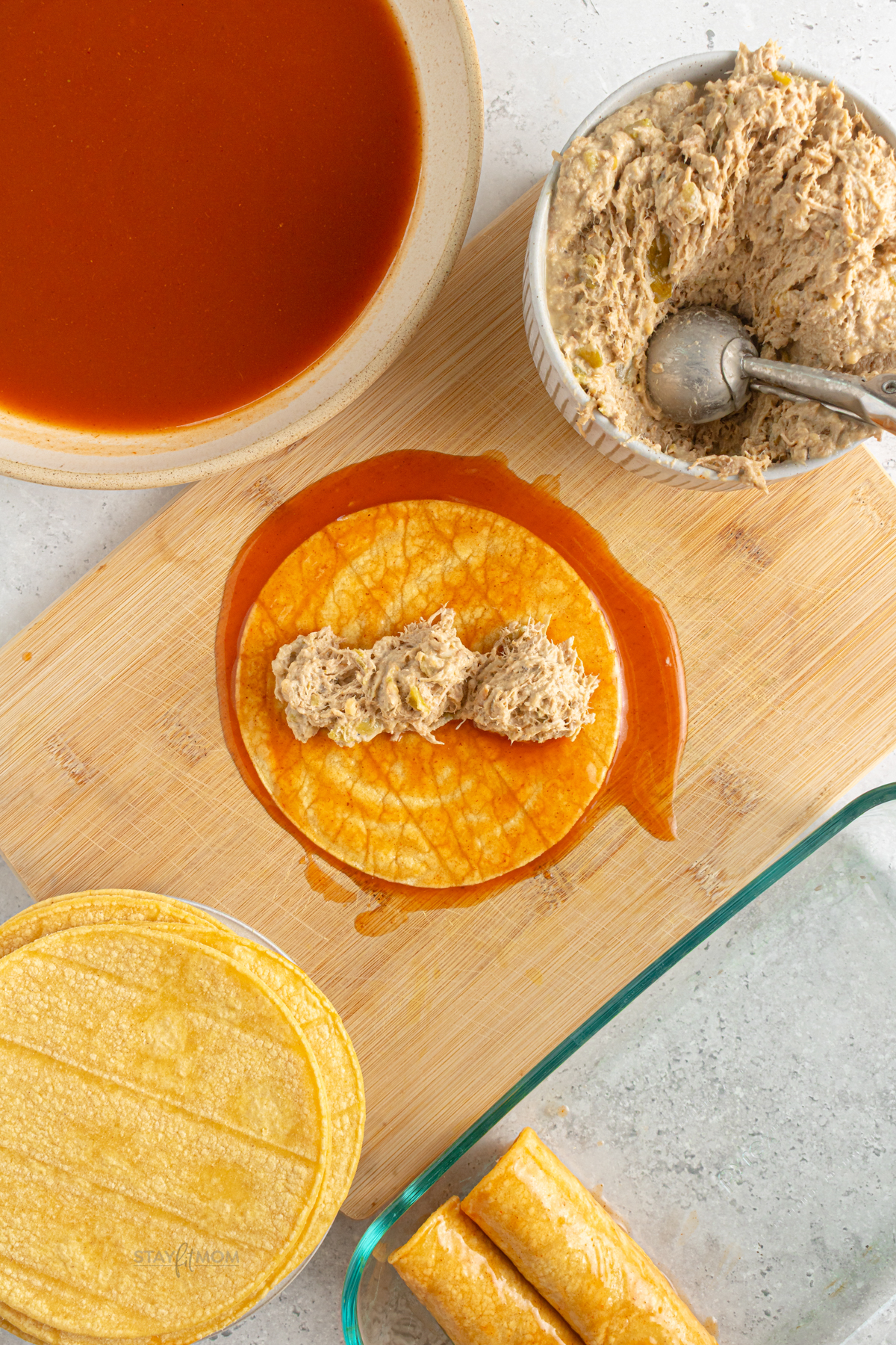 Corn tortillas coated in red enchilada sauce being filled with pork mixture before rolling for baking.