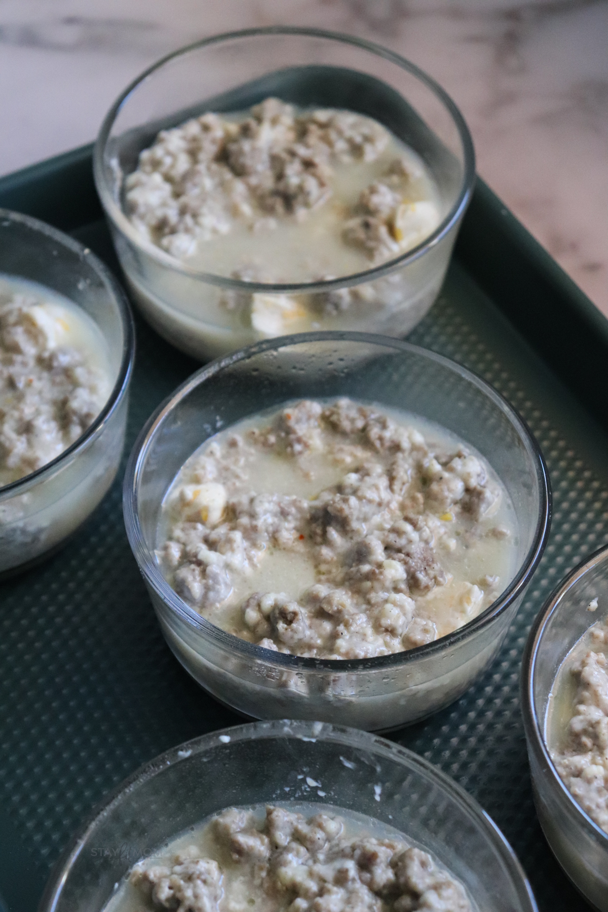 Biscuits and gravy casseroles showing oven safe containers filled with biscuits cut up and topped with egg whites and sausage gravy.