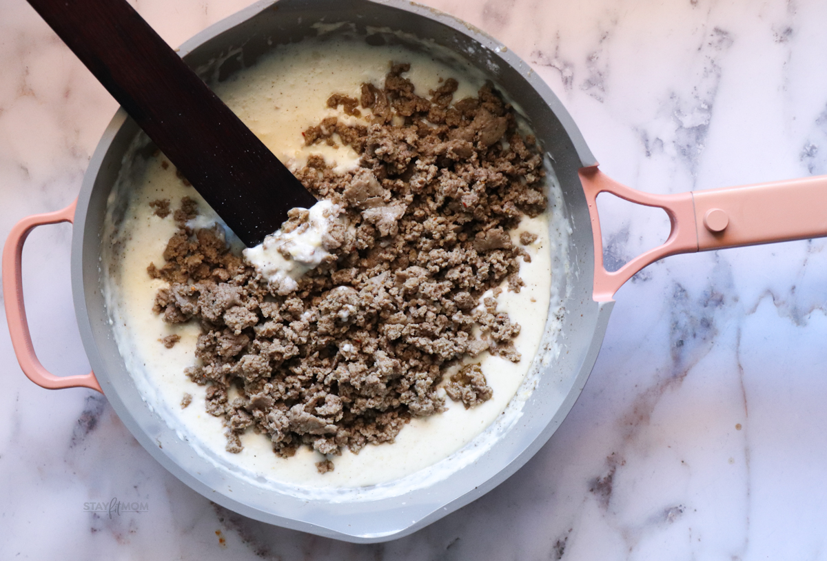 Biscuits and Gravy Casseroles showing cooked turkey sausage being stirred into the white gravy.