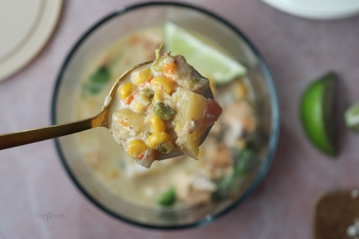 Chicken Street Corn Chowder showing a serving of soup with a spoonful raised above with the perfect bite featuring potatoes, chicken, corn, diced veggies, and broth.