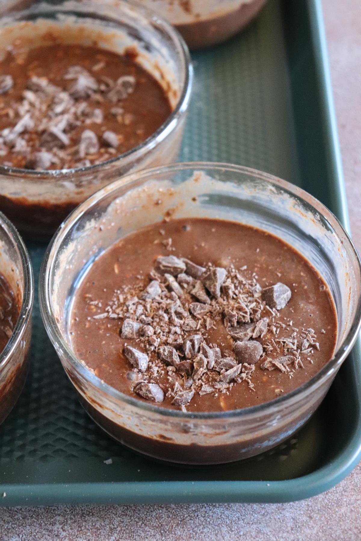 Close up of glass meal prep bowls with chocolate baked oats mixture topped with chocolate and ready to be baked.