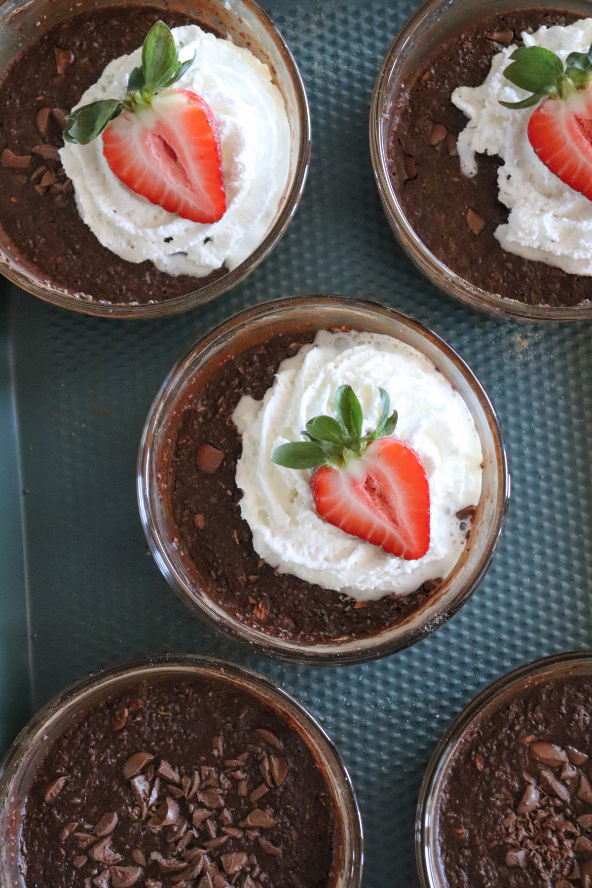 Chocolate baked oats showing completed recipe with glass meal prep bowls filled with baked oats, topped with chocolate, whipped cream, and a strawberry slice.