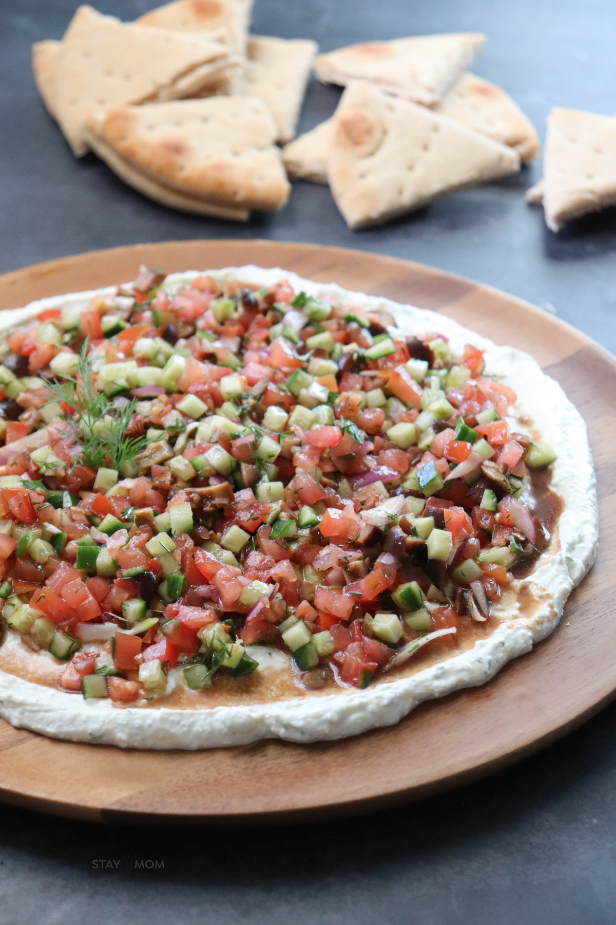 Greek Whipped Feta Dip showing completed recipe on a wooden platter with a layer of whipped feta topped with diced veggies,.