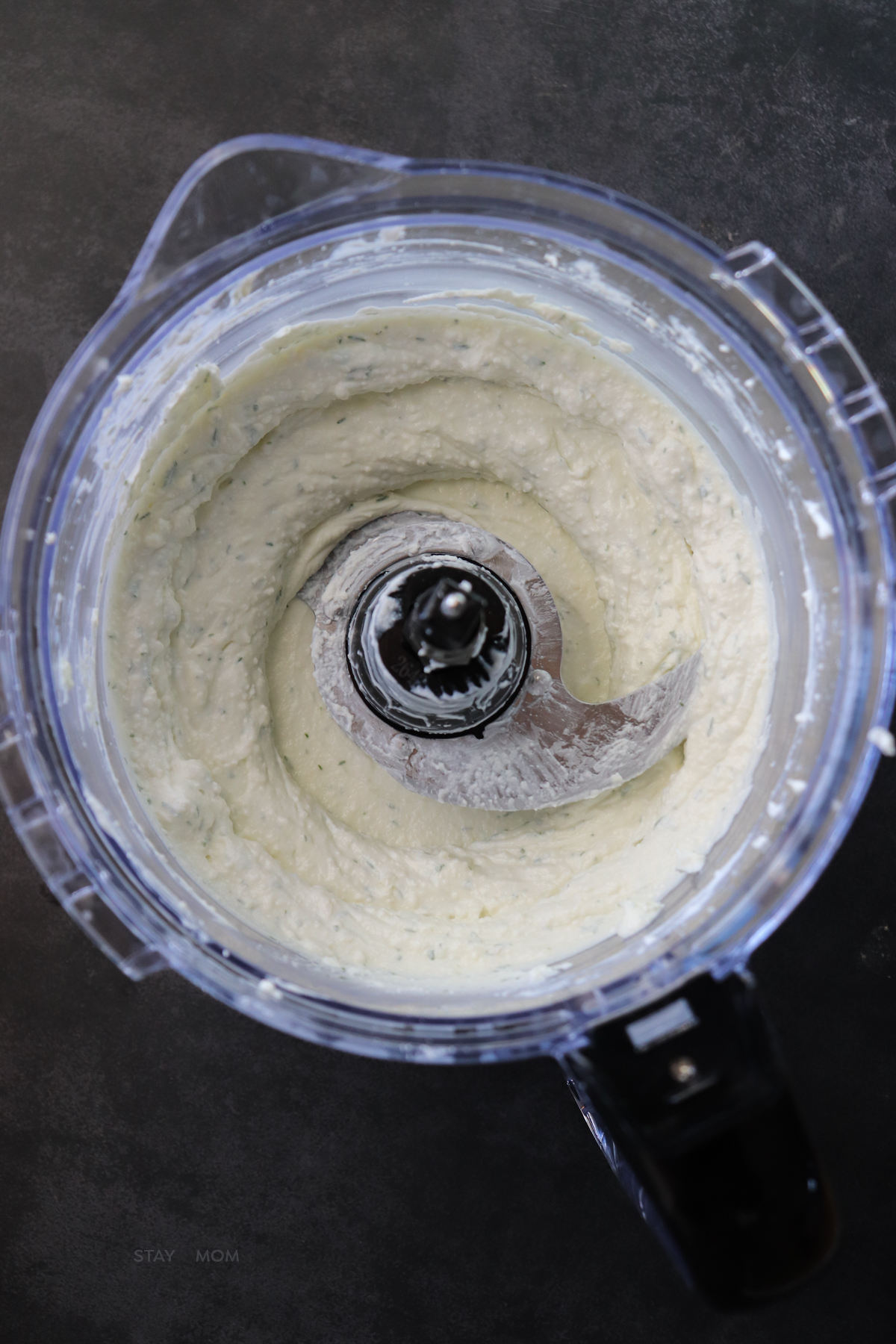 Food processor showing whipped feta, greek yogurt, garlic, lemon, and dill blended together.