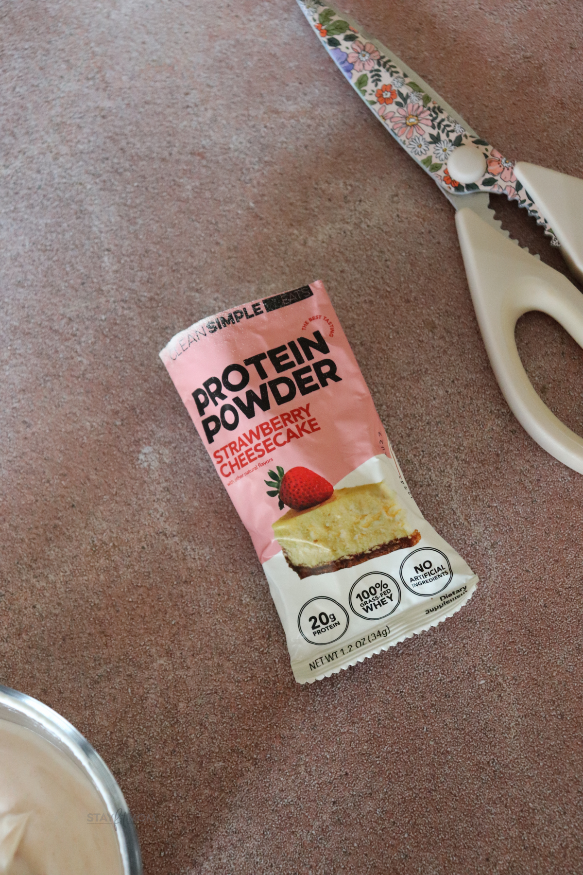 Strawberry cheesecake Clean Simple Eats protein powder packet cut open and next to a pair of scissors.