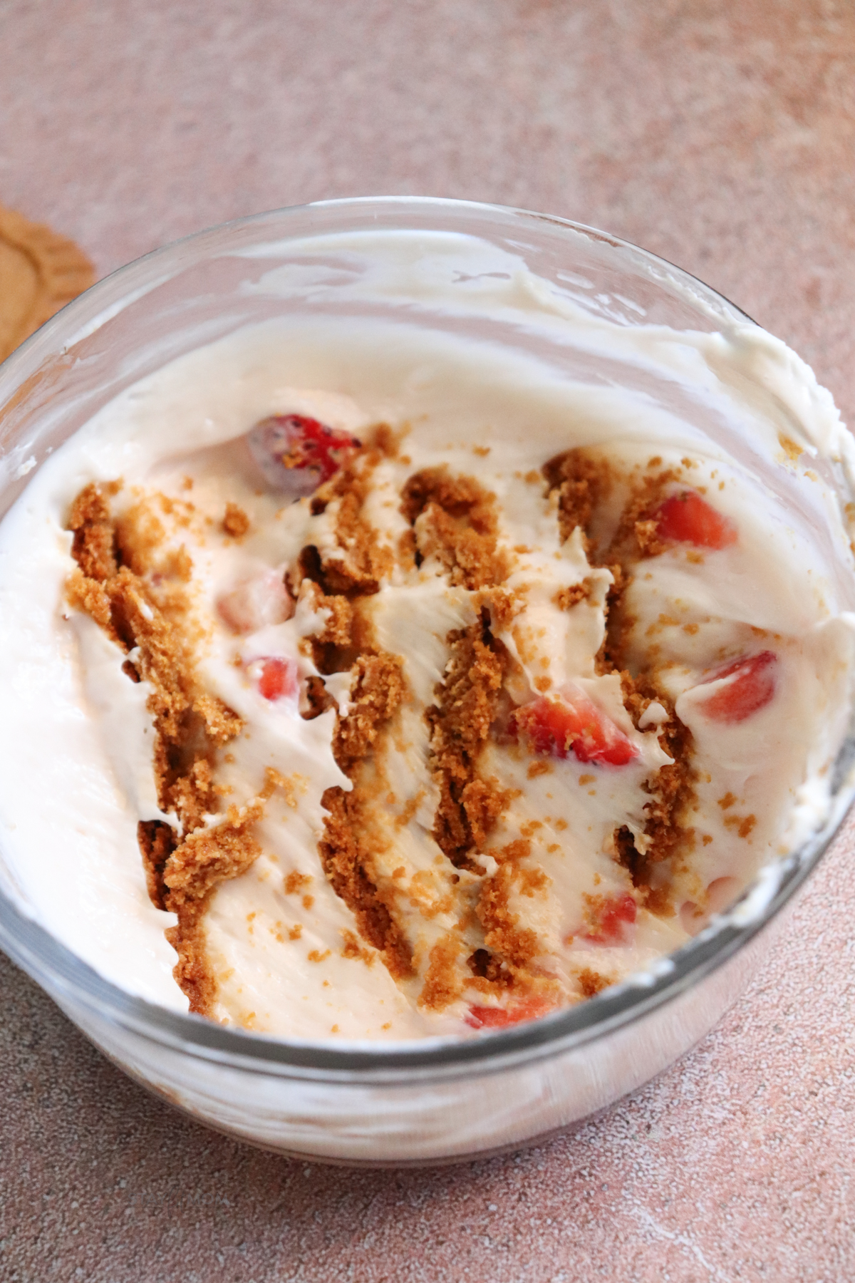 Protein Cheesecake for One showing a glass bowl with greek yogurt, strawberries, and Biscoff cookies with the top layer skimmed off so the inside is visible.
