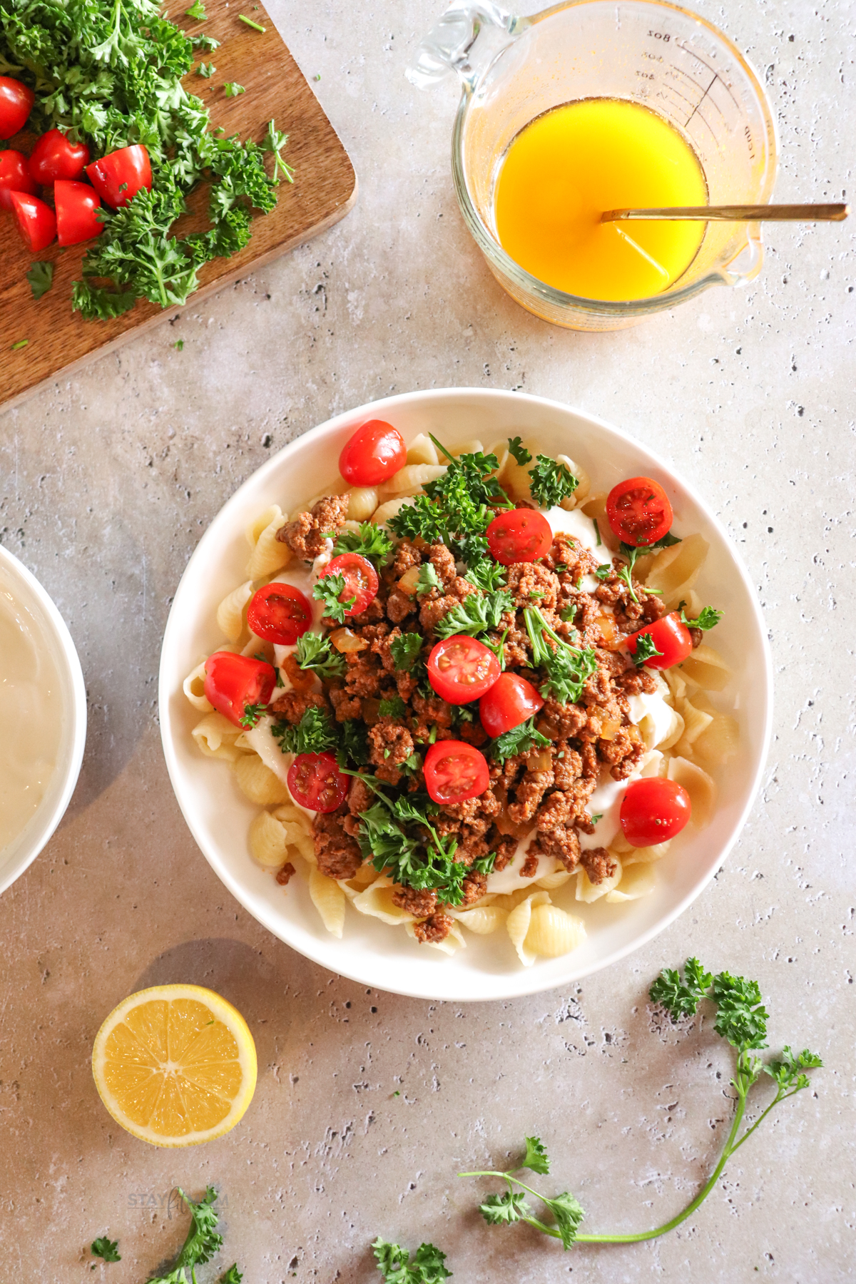 Turkish pasta showing finished recipe in a bowl with visible shell pasta, cooked ground turkey, sliced cherry tomatoes, white sauce, and garnished with parsley.