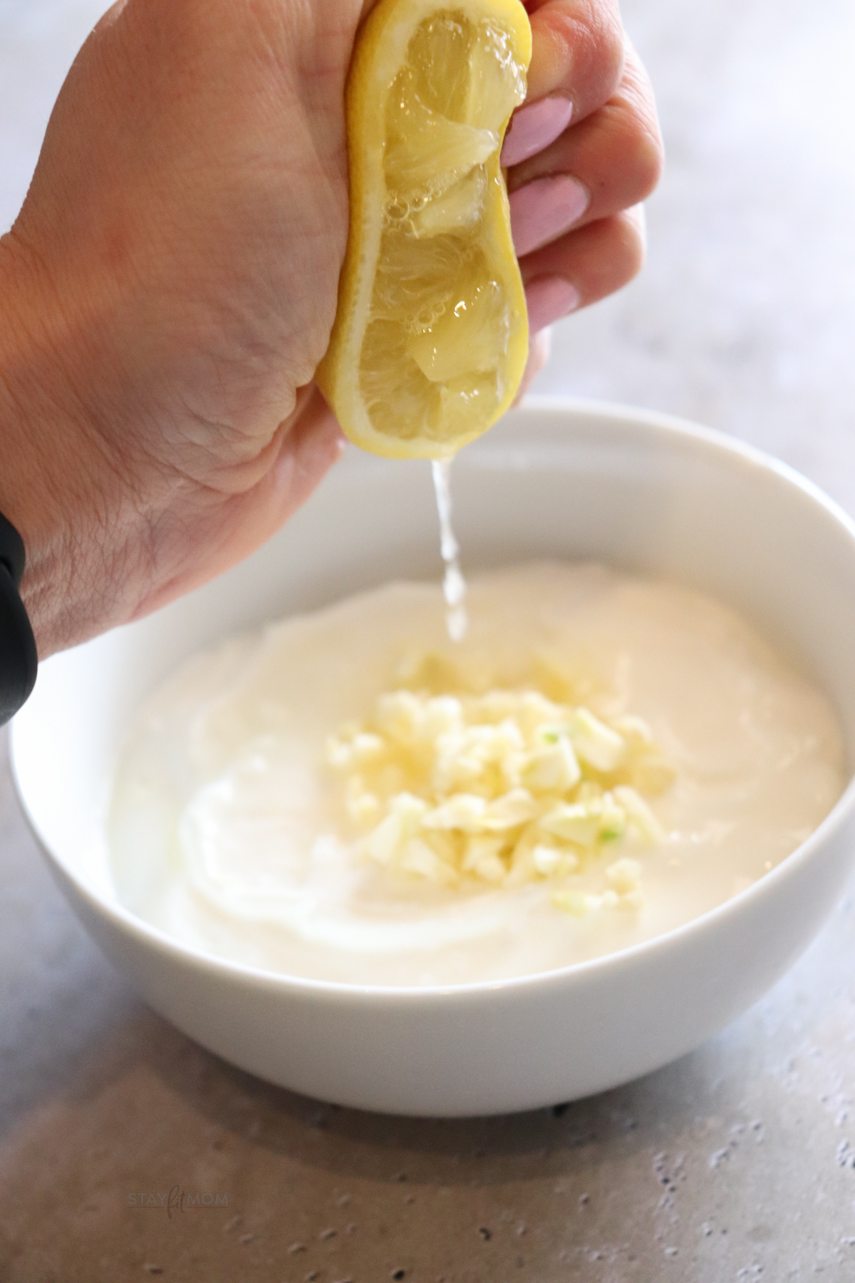 Lemon juice being squeezed into a bowl of greek yogurt, minced garlic, and salt to make the creamy sauce.