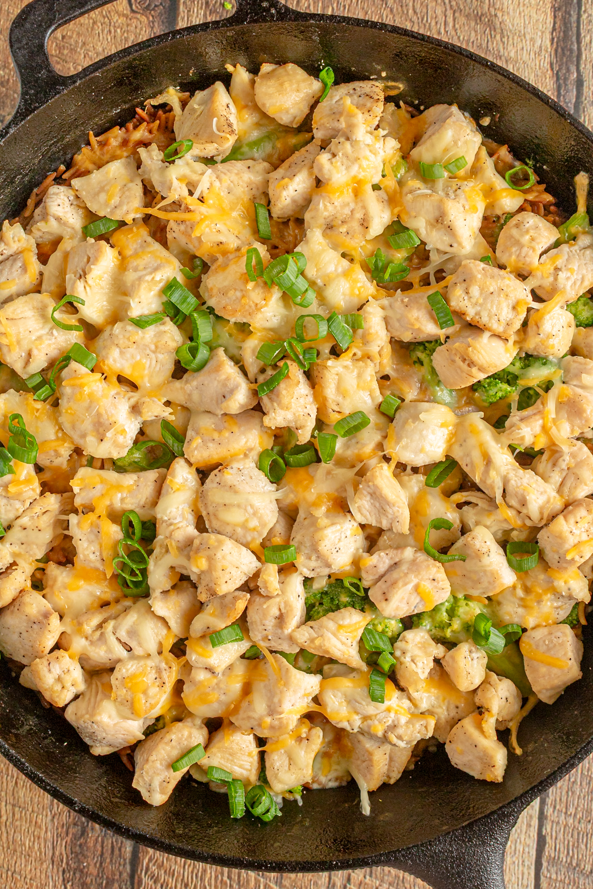 Broccoli cheddar chicken orzo showing an image of a skillet with the complete recipe with visible orzo, chicken breast, broccoli, and melted cheese.