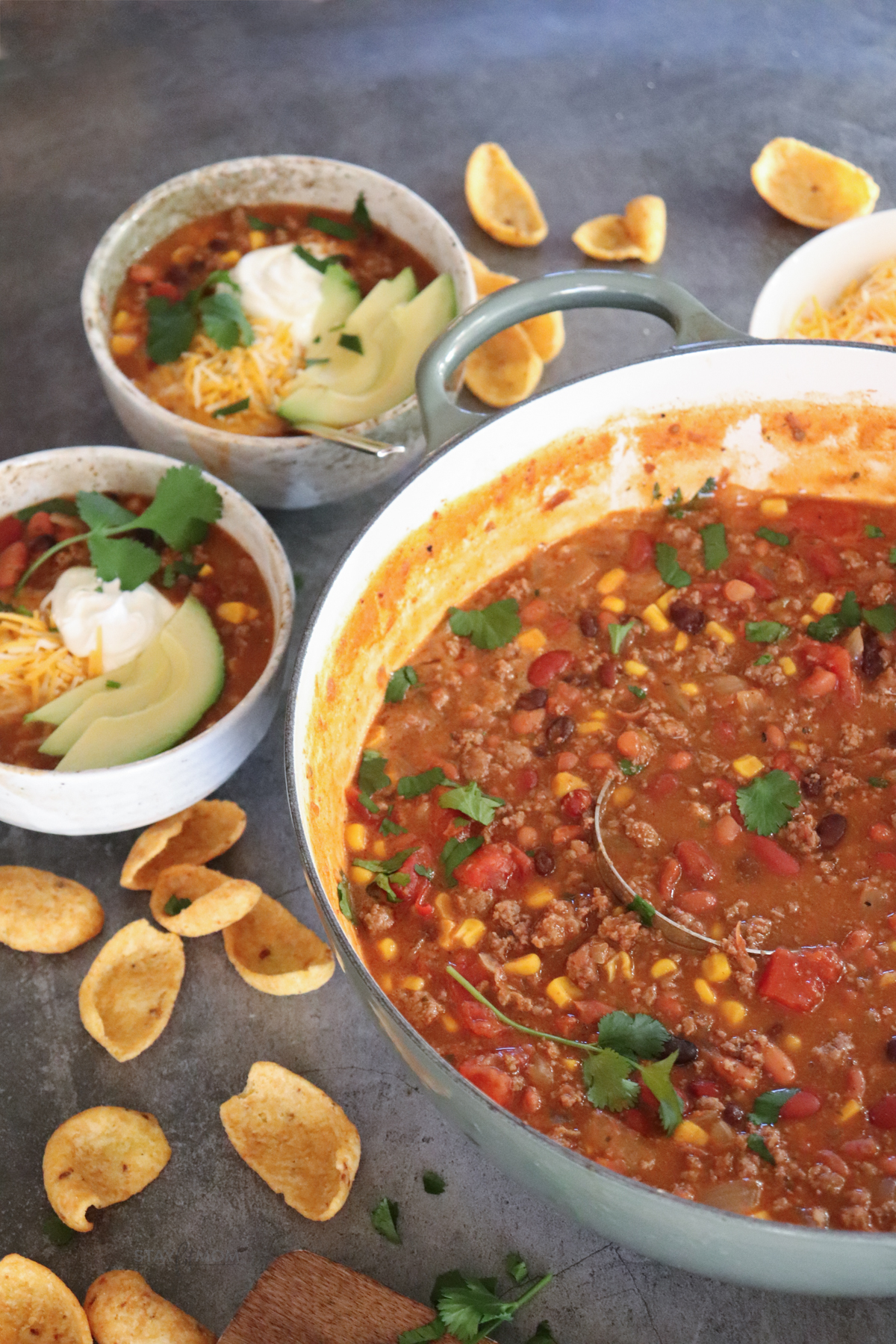 A pot of taco soup on the right with two servings shown on the left and some corn chips.