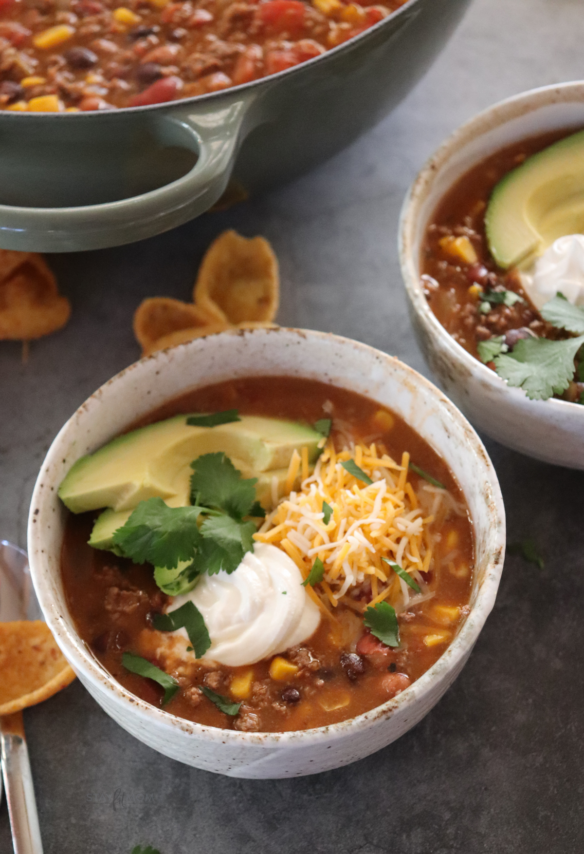 Taco Soup showing completed recipe with a serving size in a bowl topped with avocado greek yogurt, shredded cheese, and cilantro.