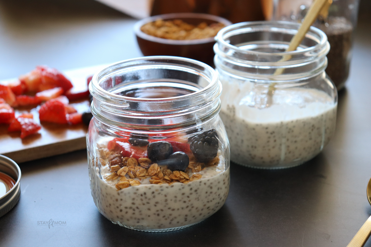 A jar of vanilla chia pudding topped with granola and berries and another jar with just the chia pudding. Fresh berries and granola are in the background.