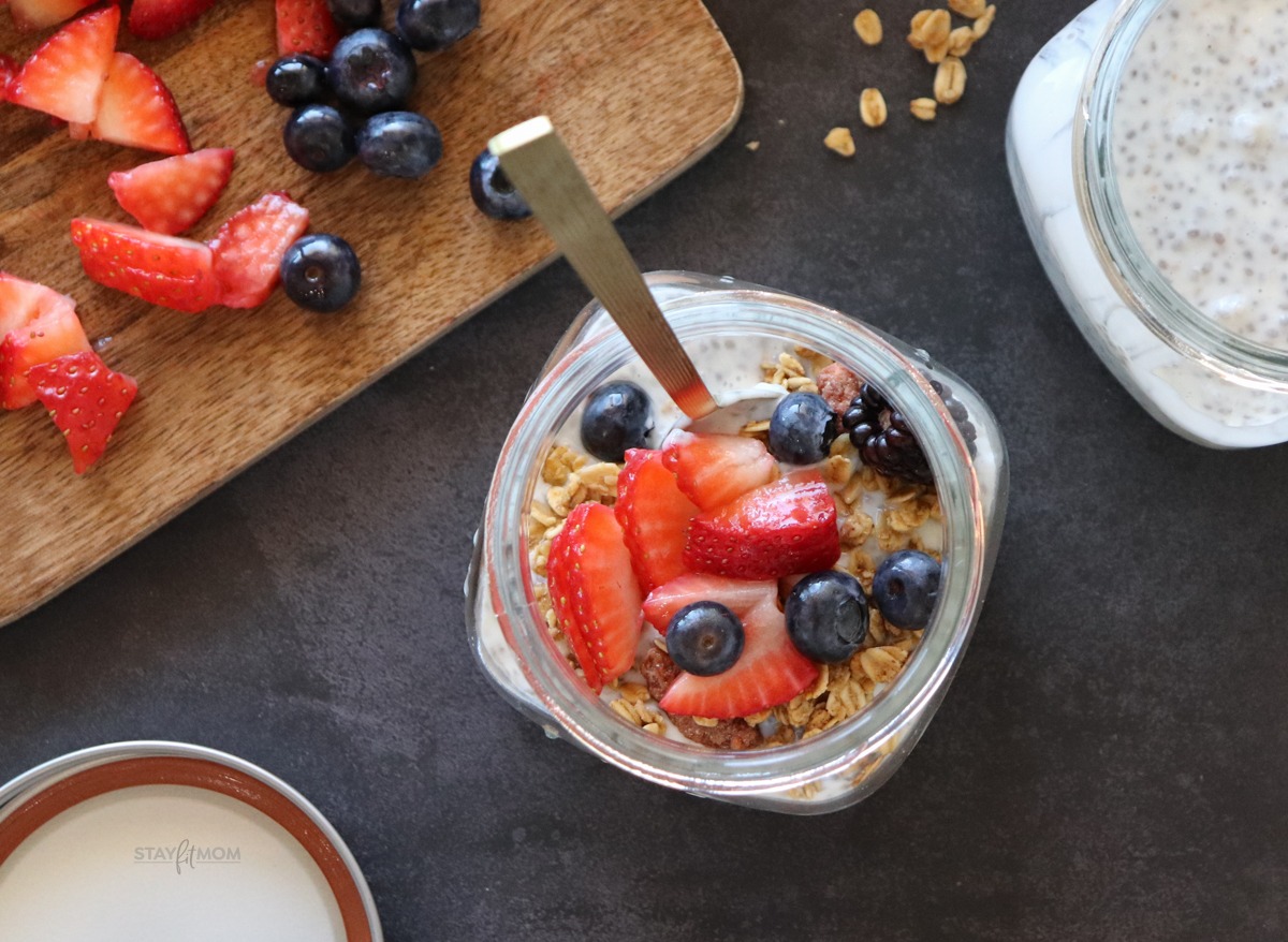 A top view of Vanilla Chia Pudding showing completed recipe in a small jar topped with fresh berries and granola with a spoon in the jar and fresh berries and granola in the background.