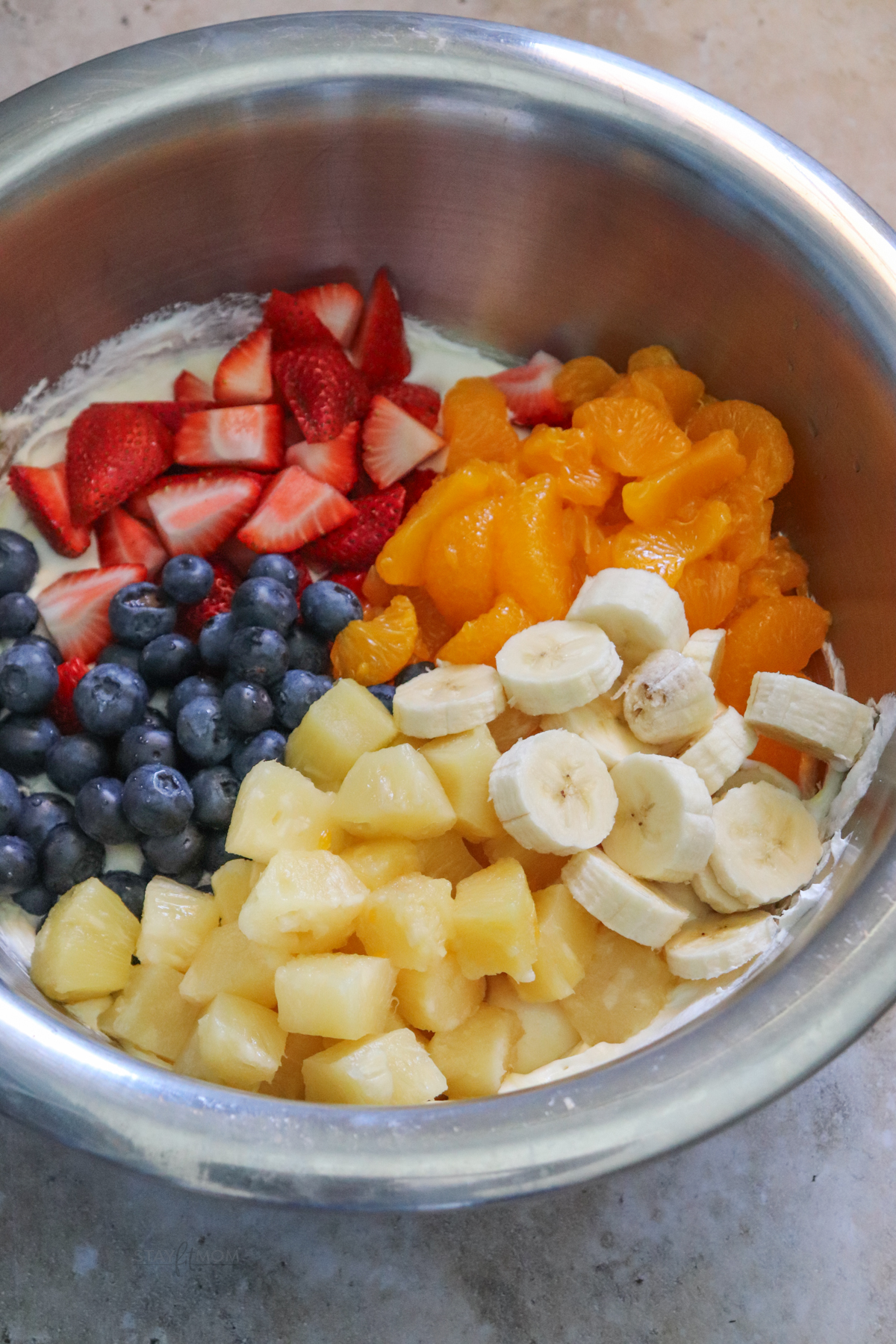 Cookie fruit salad showing silver bowl with pudding mixture in the bottom topped fruit ready to be stirred in.