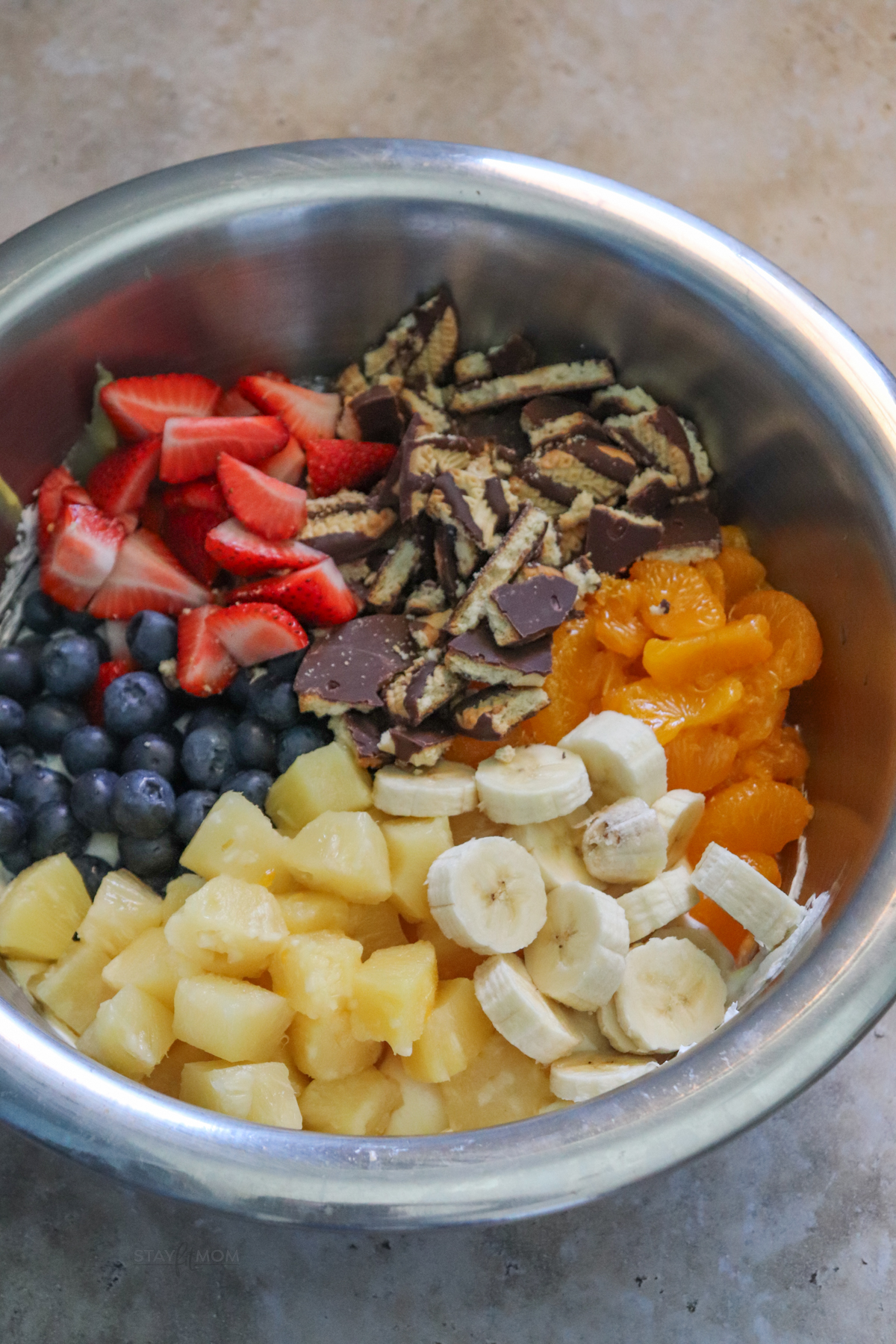 Cookie fruit salad showing silver bowl with pudding mixture in the bottom topped with cookies and fruit ready to be stirred in.